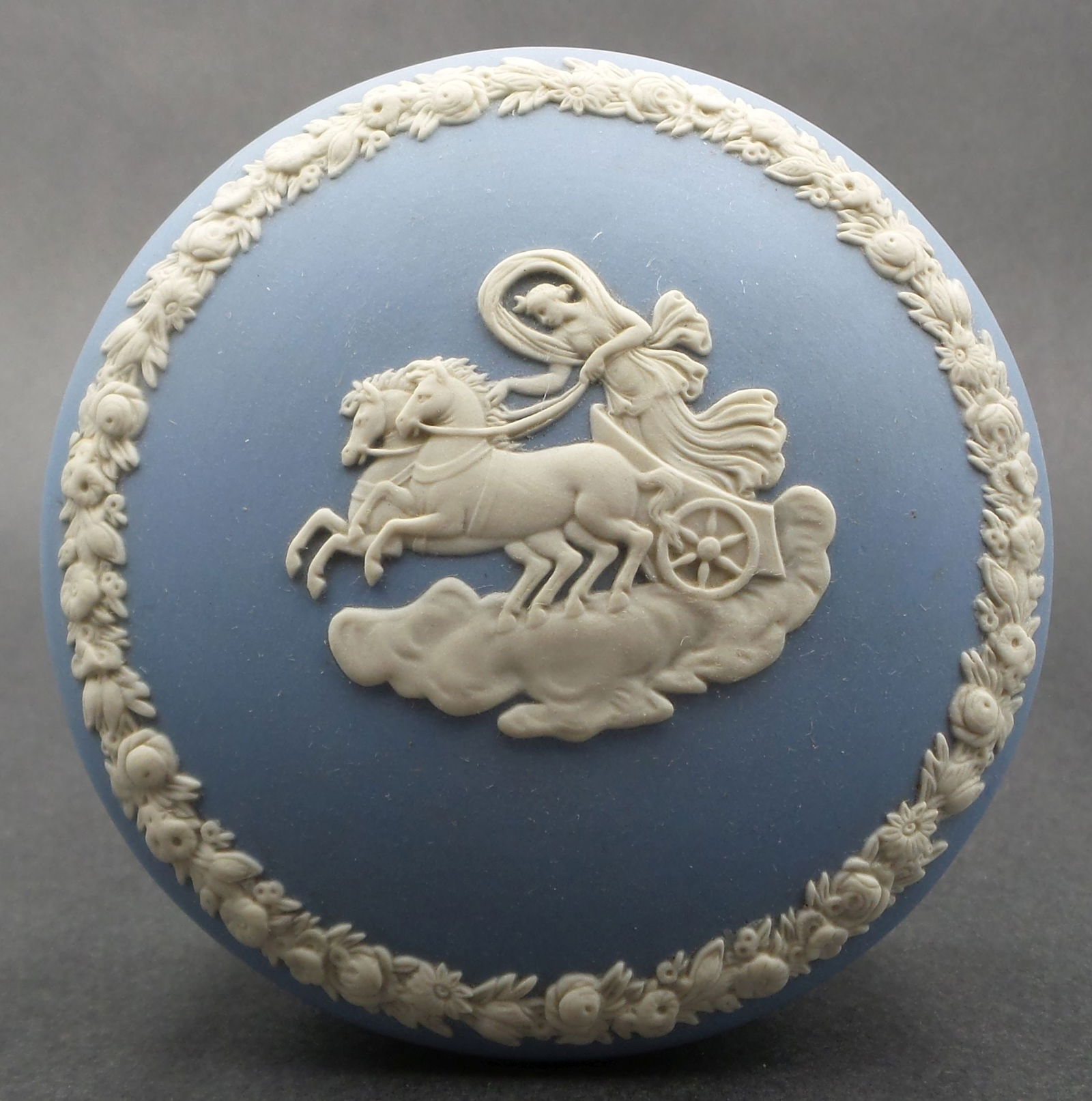 Vintage WEDGWOOD Jasperware Blue Neoclassical Lidded Trinket Box: A beautiful round blue Wedgwood trinket box with raised neoclassical motif and scrolling floral design to lid. Marked "Wedgwood Made in England." Measures approx. 3 3/4" in diameter x 2" high. Very go