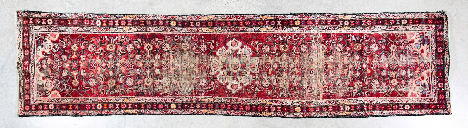 A Persian Runner Rug: Extensively worn, with areas of loss, floral and geometric patterns over a red field, 20th Century, 9' 11" x 2' 5".