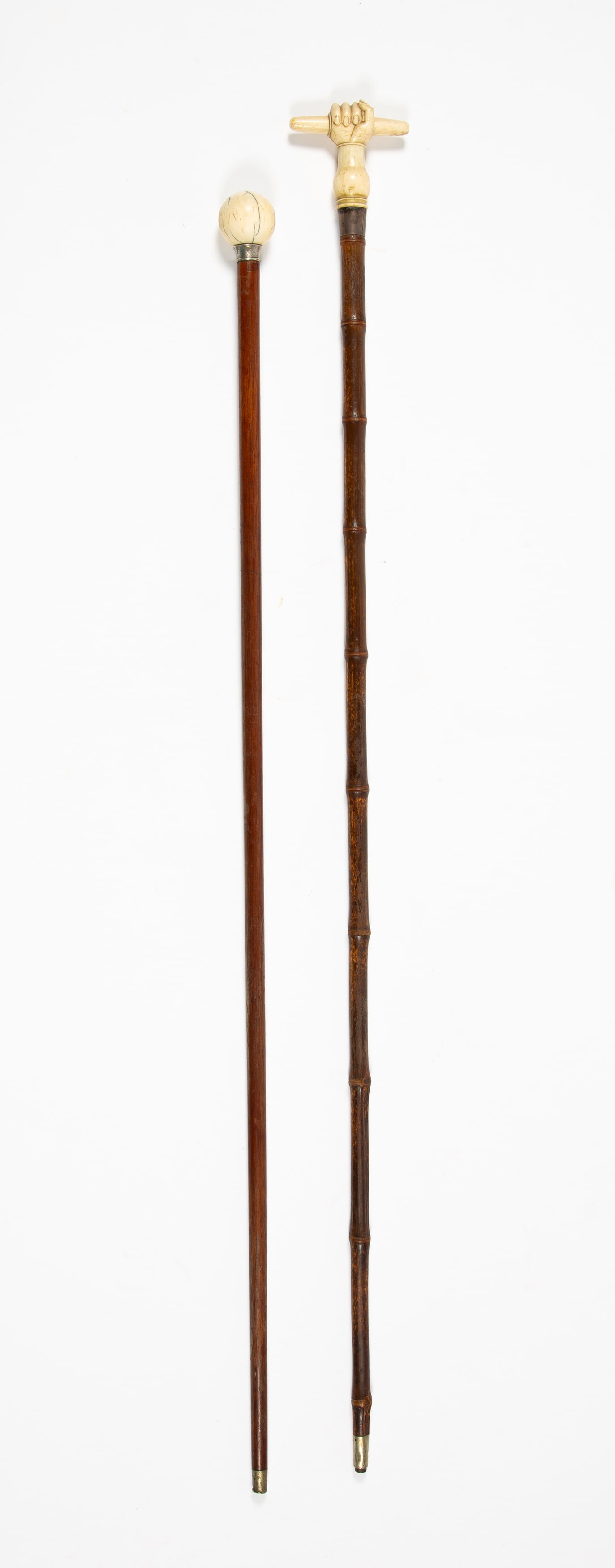 Two Antique Carved Bone Handled Canes: The first a clenched fist holding a rod, with silver flange hallmarked for London and sterling with the makers mark "F.B" above tapered bamboo shaft with silver terminus, 35" long, the other a knob st