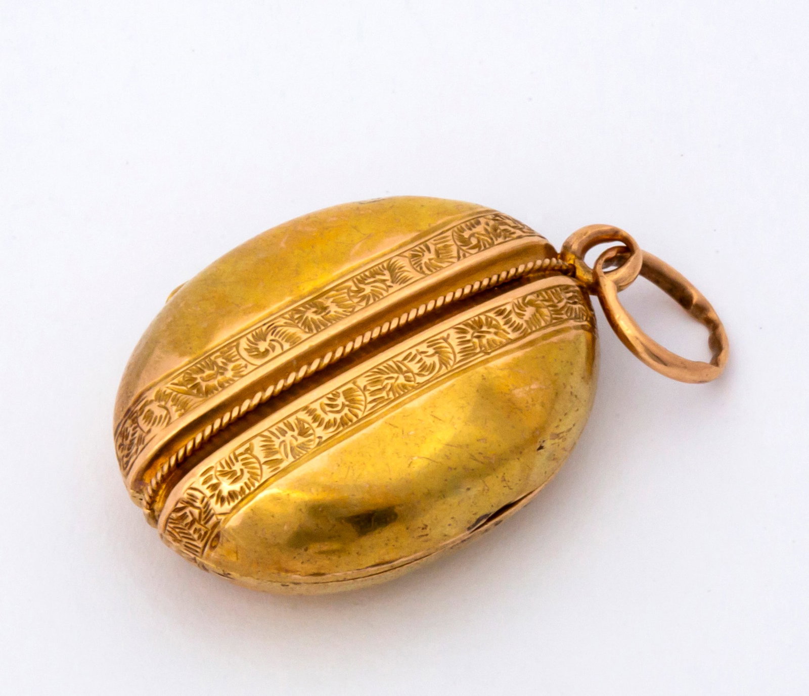 An Antique 18K Gold Locket: Spectrometer tested, oval locket with center rope detail and engraved banding, the locket is in restoration condition with the hinge currently separated from one side but still closes and can be used,