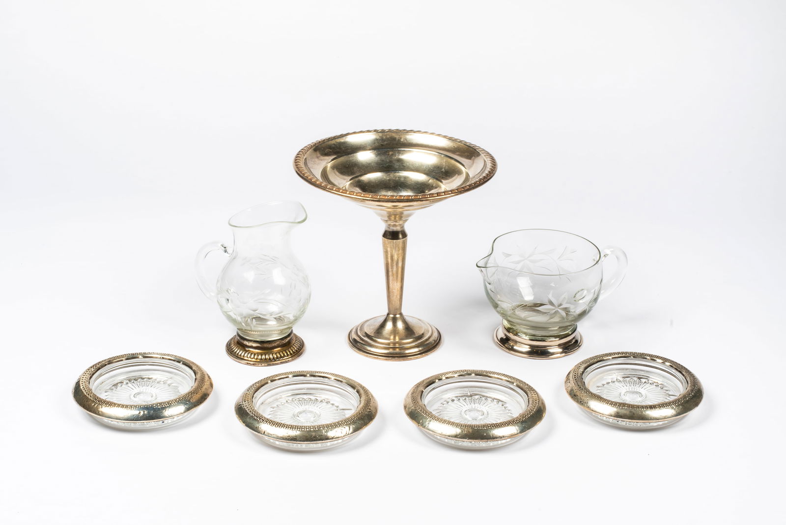 A Group of Sterling and Glass Tableware: Includes: a set of four glass coasters with sterling edges; a tall sterling weighted compote; and two cut glass pitchers with sterling foots. 