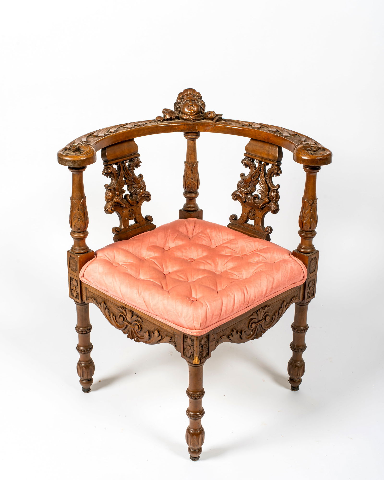 An Italian Renaissance Revival Antique Corner Chair: Of walnut, with two piece curved back with applied winged cherub to top rail and carved foliate designs across the arms, curving up and around to form hand holds; back splats with well carved fi