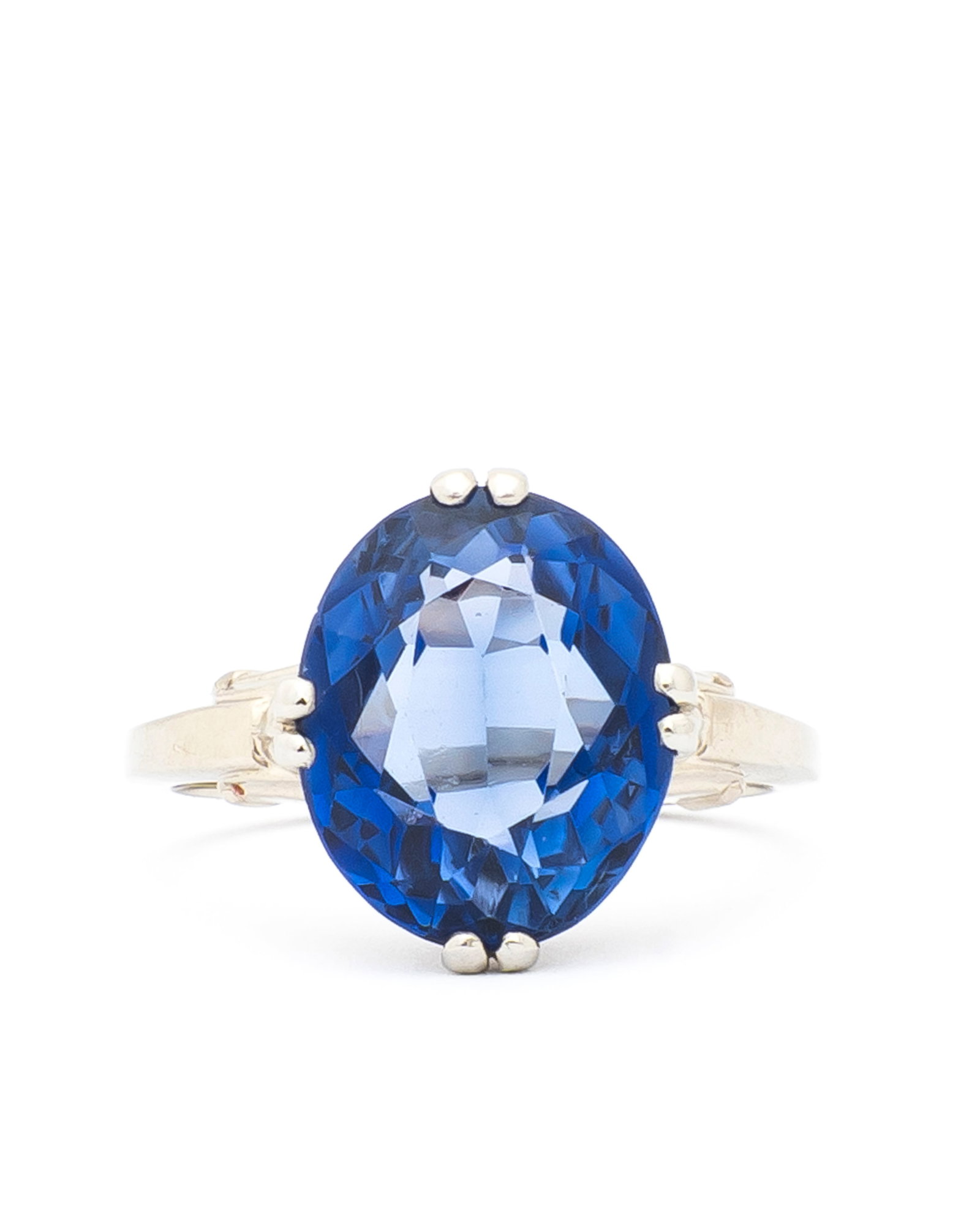 A 14K Gold and Sapphire Ring: Marked, "k14", a roughly 12mm x 10mm oval vibrant blue synthetic sapphire held with four sets of double prongs, raised shoulders and a pierced gallery, a ring size of 5 1/2- 3/4 and a total weight of