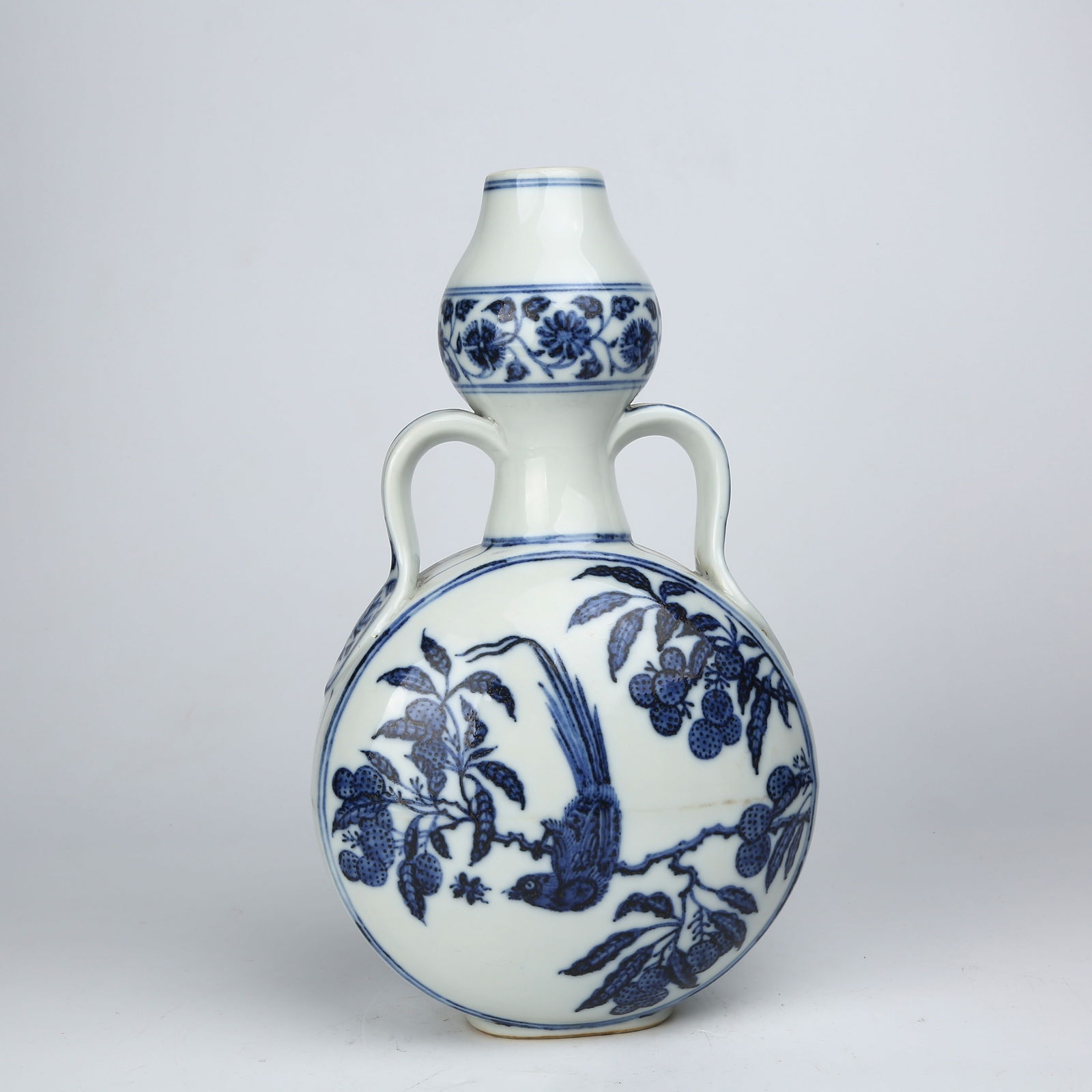 A BLUE-AND-WHITE BIRD-AND-FLOWER PATTERN GOURD VASE WITH RIBBON HANDLES: Blue-and-white bird-and-flower pattern gourd vase with ribbon handles