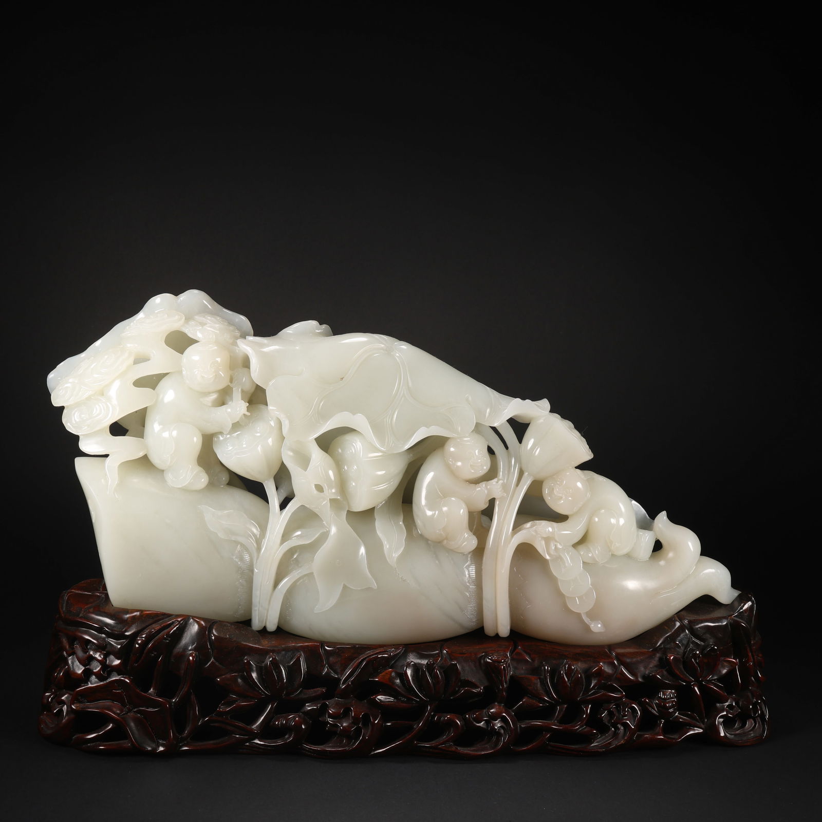A HETIAN JADE FIGURINE OF CHILD PLAYING WITH LOTUS ON WOODEN BASE (1 of 9)