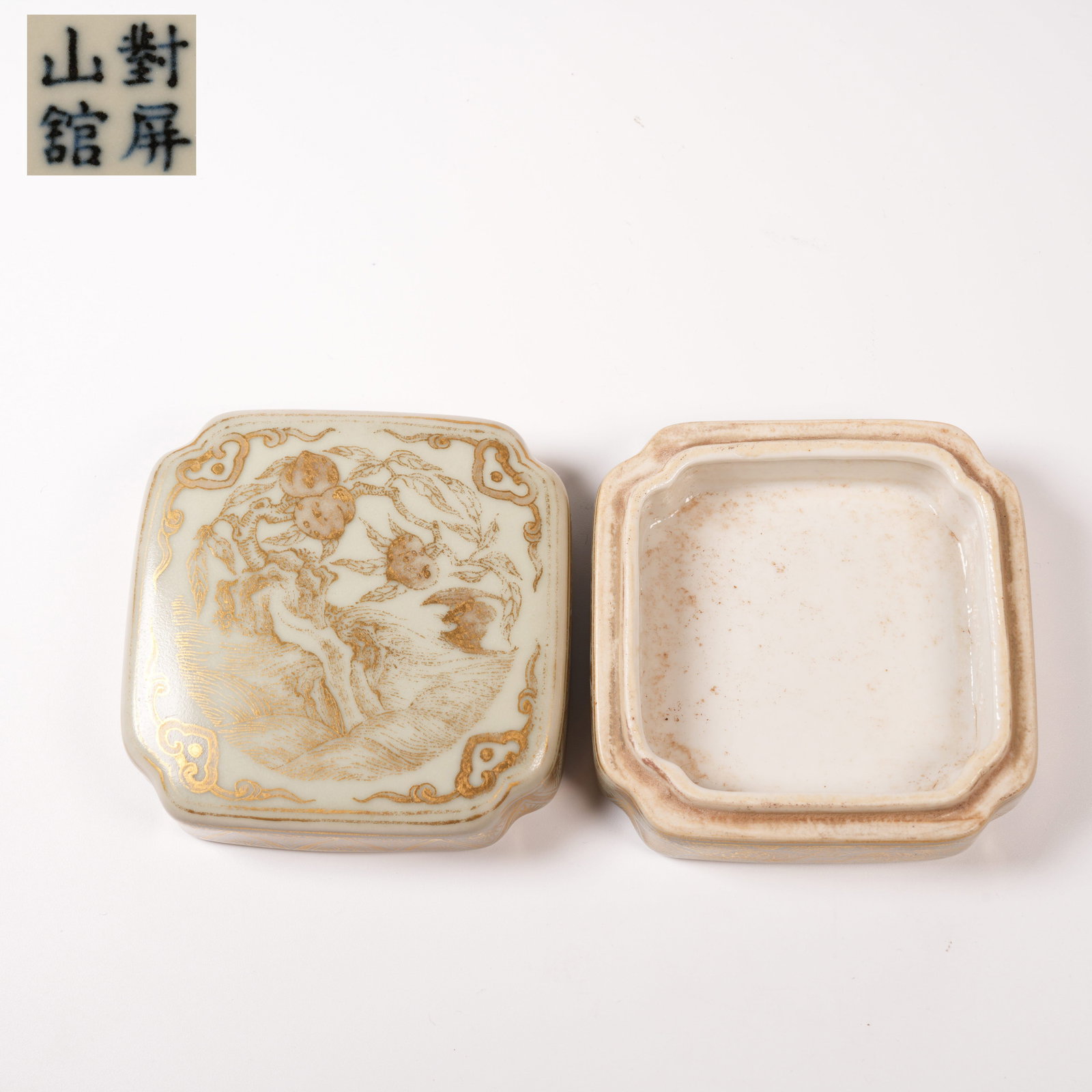 A FAMILLE ROSE-AND-CELADON SQUARE INK PASTE BOX WITH GILT AUSPICIOUS PEACH MOTIF AND CORNER LAPPETS: Famille rose-and-celadon square ink paste box with gilt auspicious peach motif and corner lappets