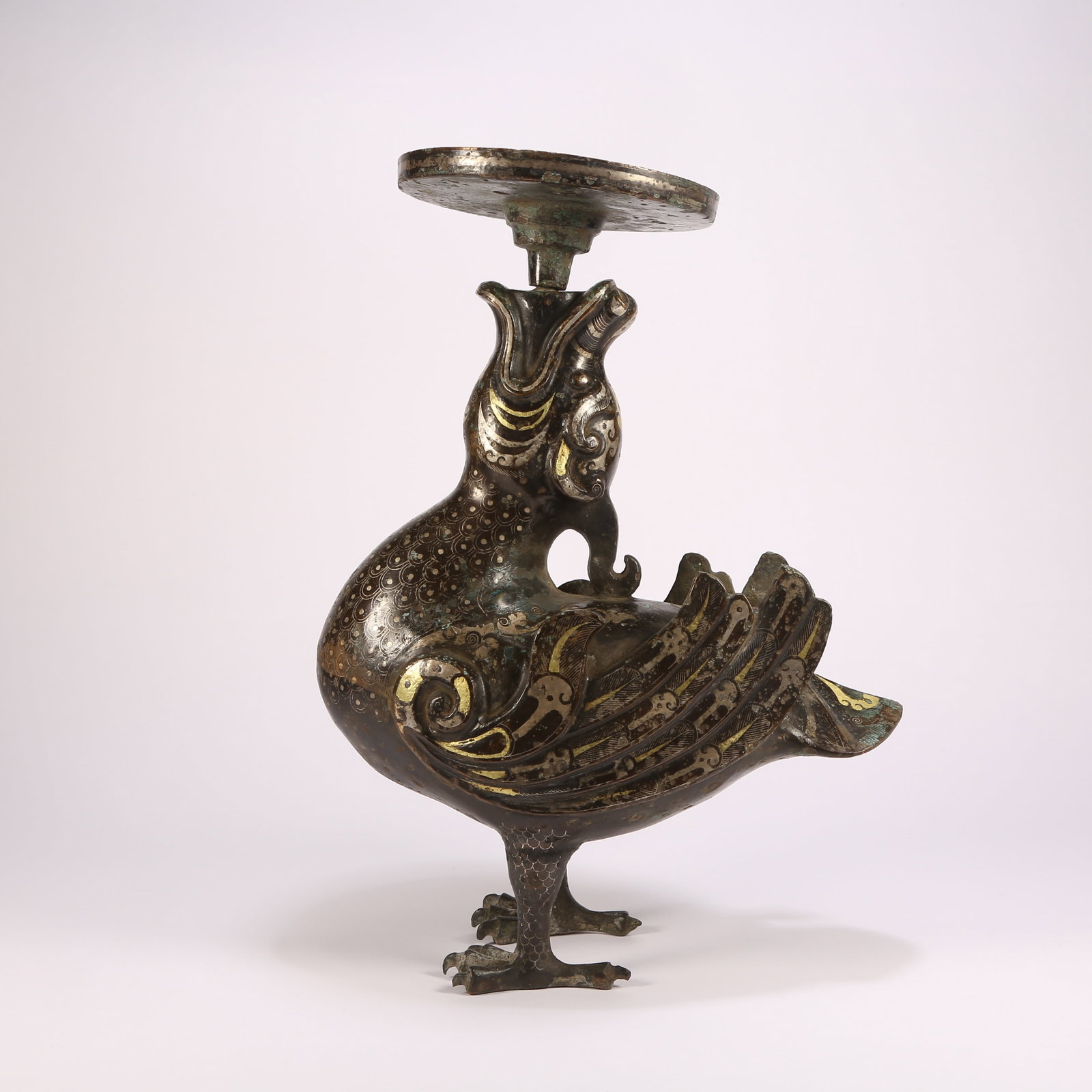 A BRONZE CANDLEHOLDER IN THE FORM OF A DIVINE PHOENIX WITH GILT-INLAID GOLD AND SILVER: Bronze candleholder in the form of a divine phoenix with gilt-inlaid gold and silver