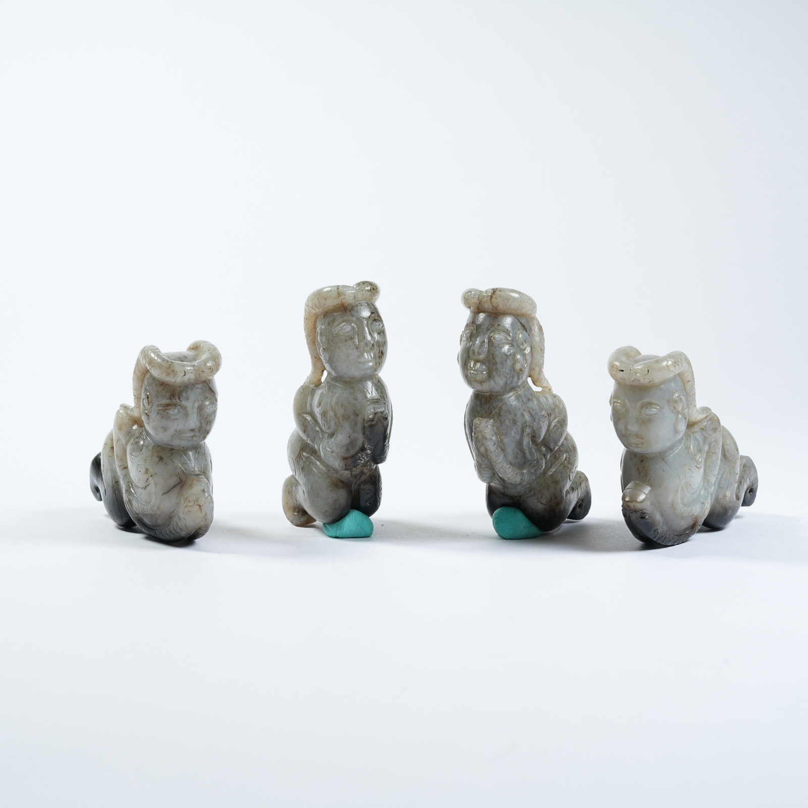 A SET OF FOUR ANCIENT JADE ORNAMENTS OF KNEELING FIGURES WITH DRAGON PATTERNS: Set of Four Ancient Jade Ornaments of Kneeling Figures with Dragon Patterns