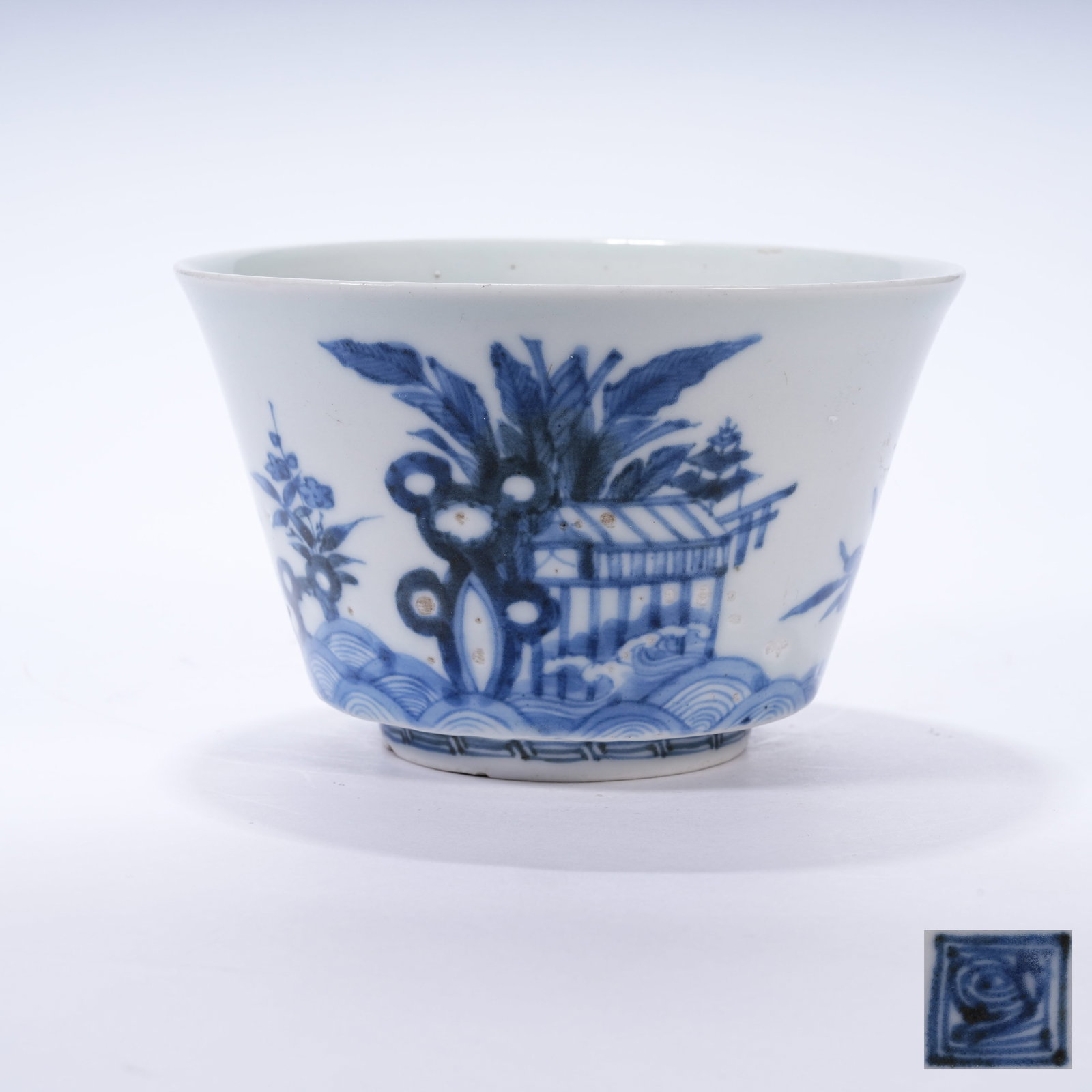 A BLUE AND WHITE CUP WITH ROCK AND FLORAL PATTERNS: Blue and White Cup with Rock and Floral Patterns