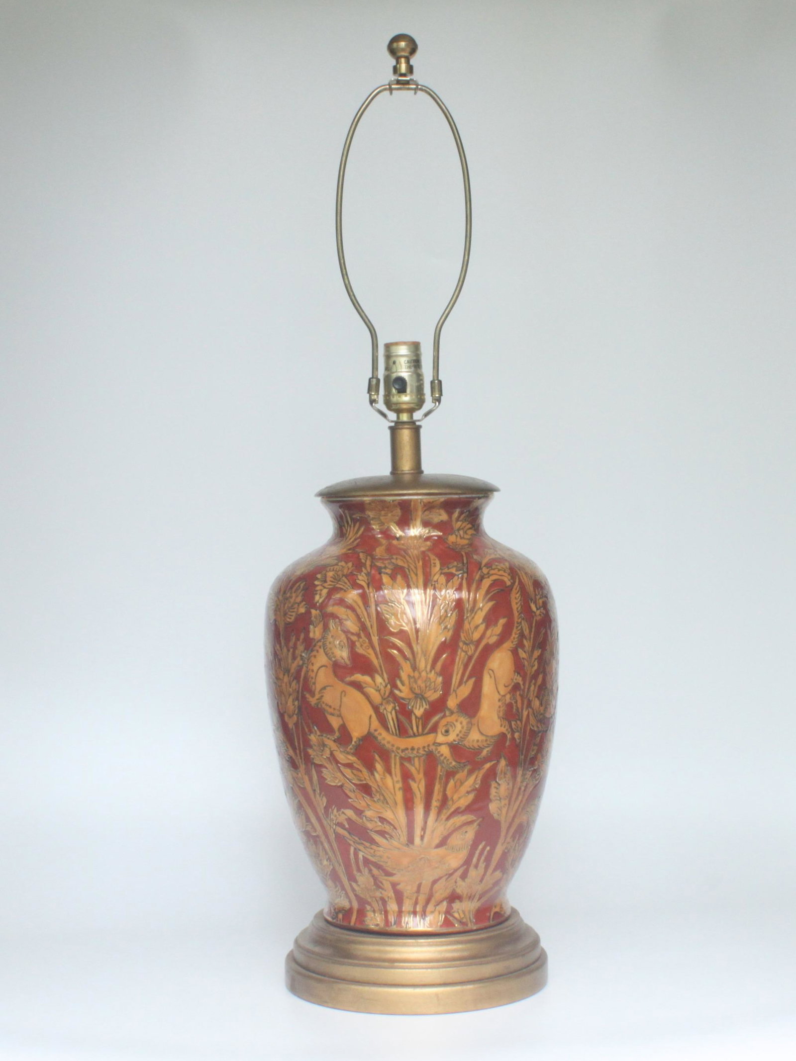 Frederick Cooper Ceramic Lamp in Warm Spice Tones: A Frederick Cooper large ceramic lamp with gold-outlined, orange flora and fauna over a rust-colored background. Mounted on a gold colored base with gold cord. Original Frederick Cooper label on the s