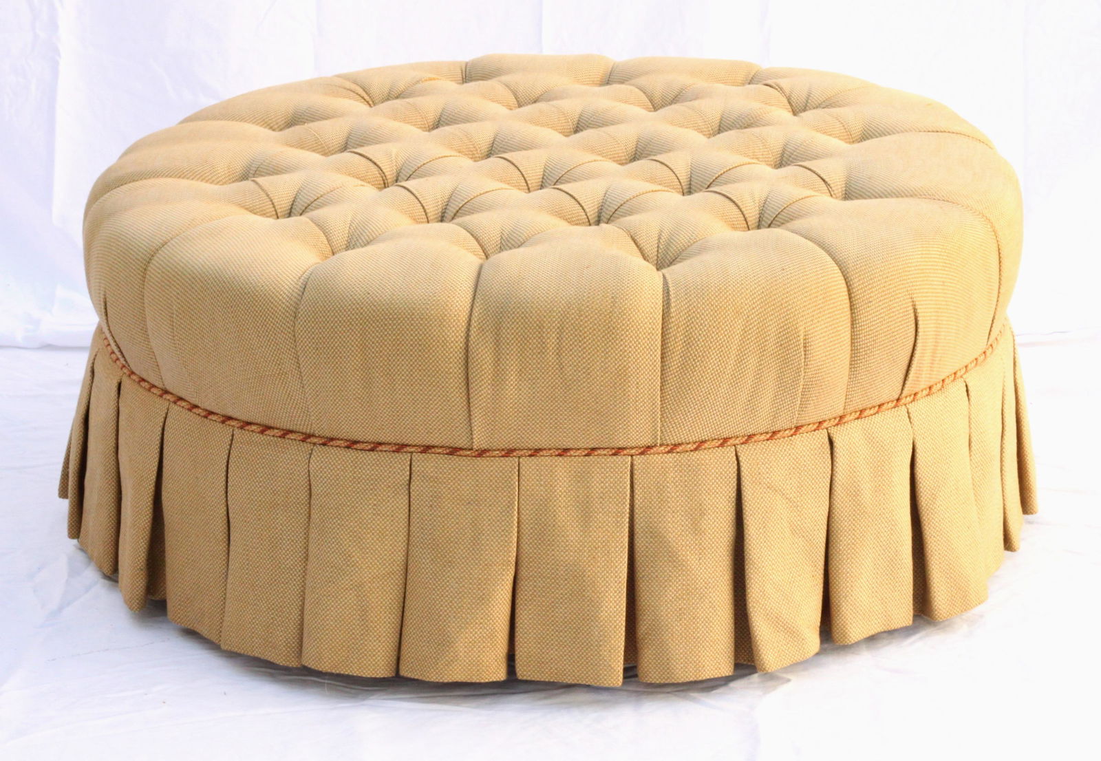 Ethan Allen Round Tufted Ottoman with Skirt, 2009: Tan basketweave fabric with tufting on top. Brown/ red/ orange cording above pleated skirt with tapered legs. Retains original lable. 37" dia. x 16" H.
