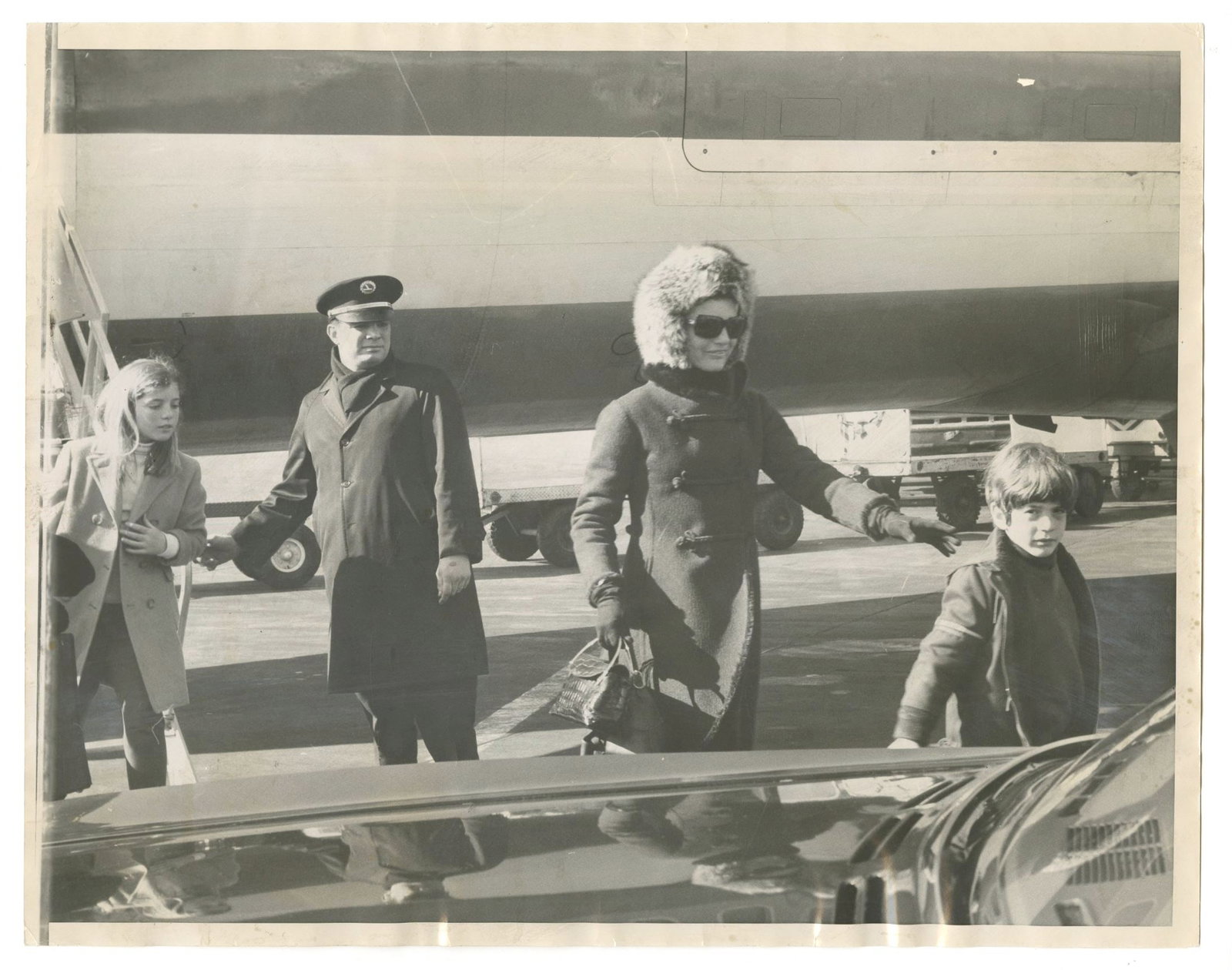 Jacqueline Kennedy with Caroline & JFK Jr. – Original Oversized 14 x 11 Press Photograph: Details: Jacqueline Kennedy original 14 x 11” black-and-white press photograph depicting her arrival with her children, Caroline Kennedy and John F. Kennedy Jr., as they disembark at JFK