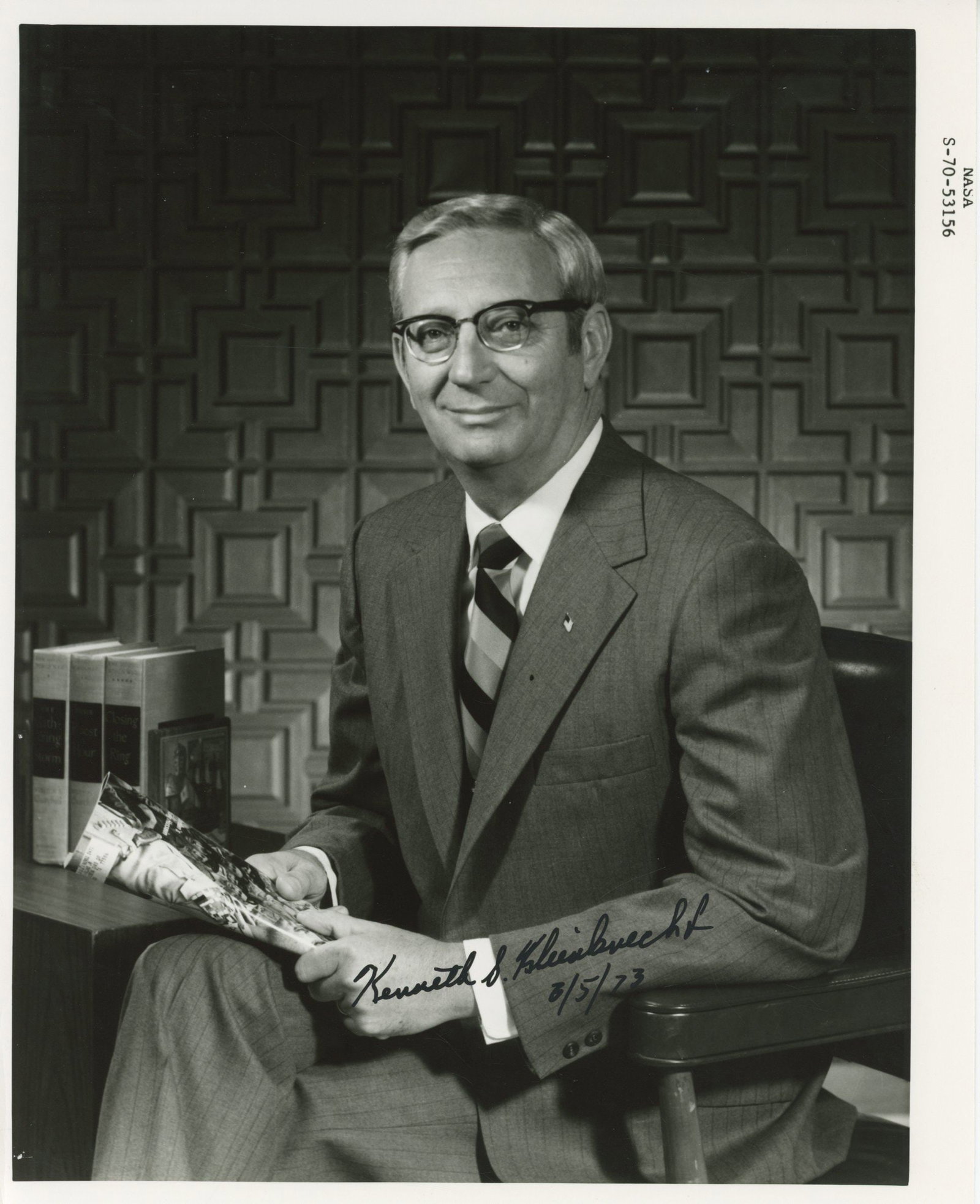 Kenneth S. Kleinknecht – Apollo Program Manager – Autographed Photograph – 8 ×: Details: Kenneth S. Kleinknecht autographed 8 × 10-inch black-and-white NASA photograph depicting the Apollo-era administrator seated in a formal office setting, holding Apollo mission imagery. T