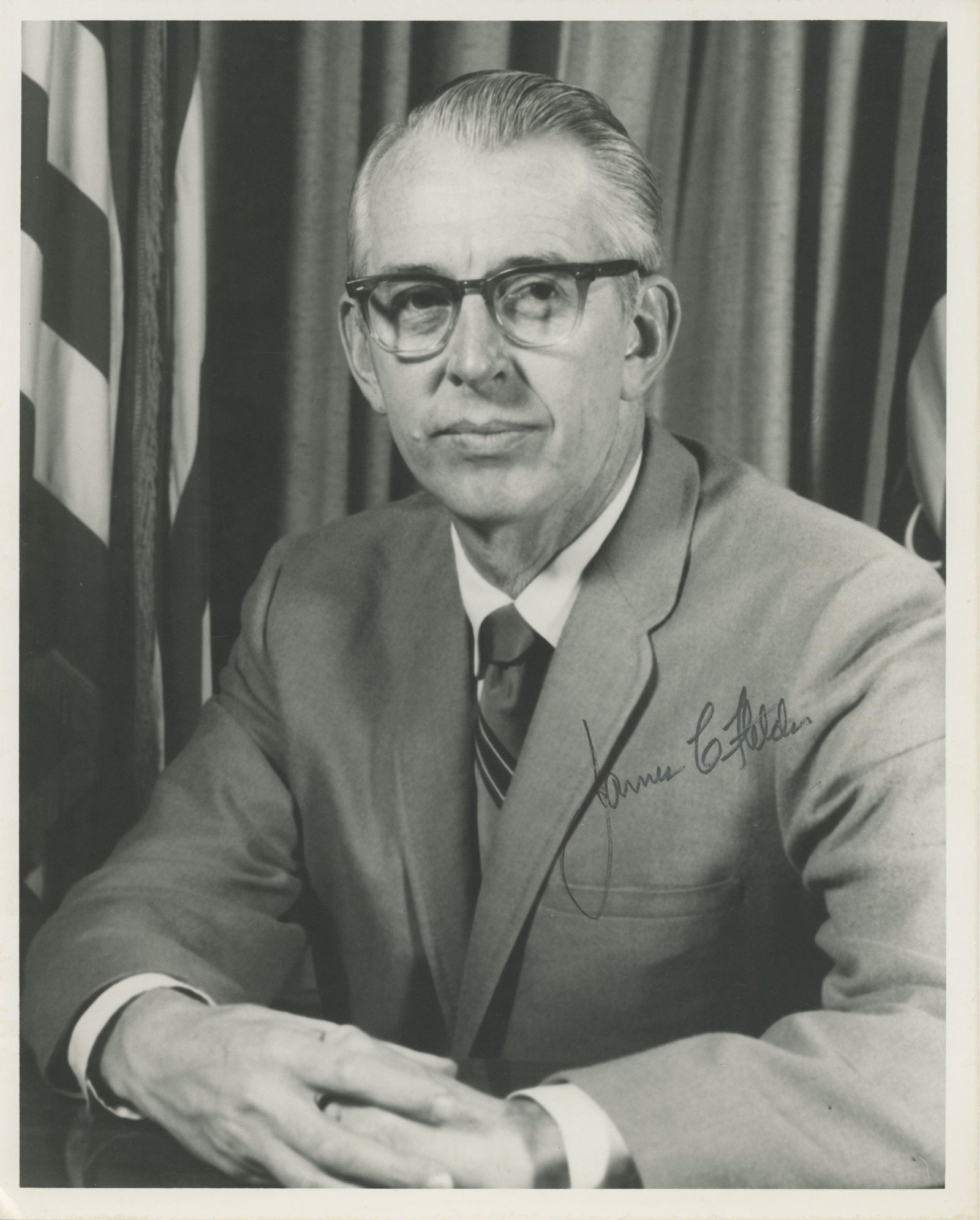 James C. Fletcher – NASA Administrator – Autographed Double-Weight Photograph – 8 : Details: James C. Fletcher autographed black-and-white double-weight photographic portrait depicting the NASA Administrator seated formally before draped flags, presenting a composed, statesmanlike im