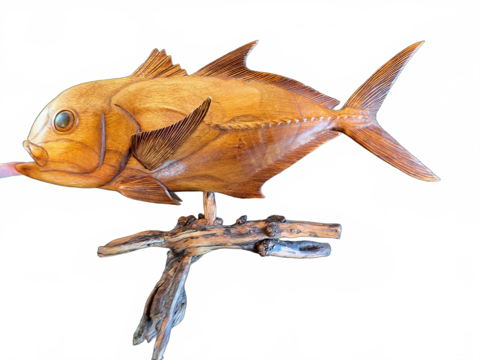 Hand-Carved Wooden Fish Sculpture on Stand: Hand-carved wooden fish sculpture of a Big Eye Jack displayed on a natural wood branch stand. Features detailed carving to represent fins, scales, and eyes, finished in a medium golden brown tone. Uni