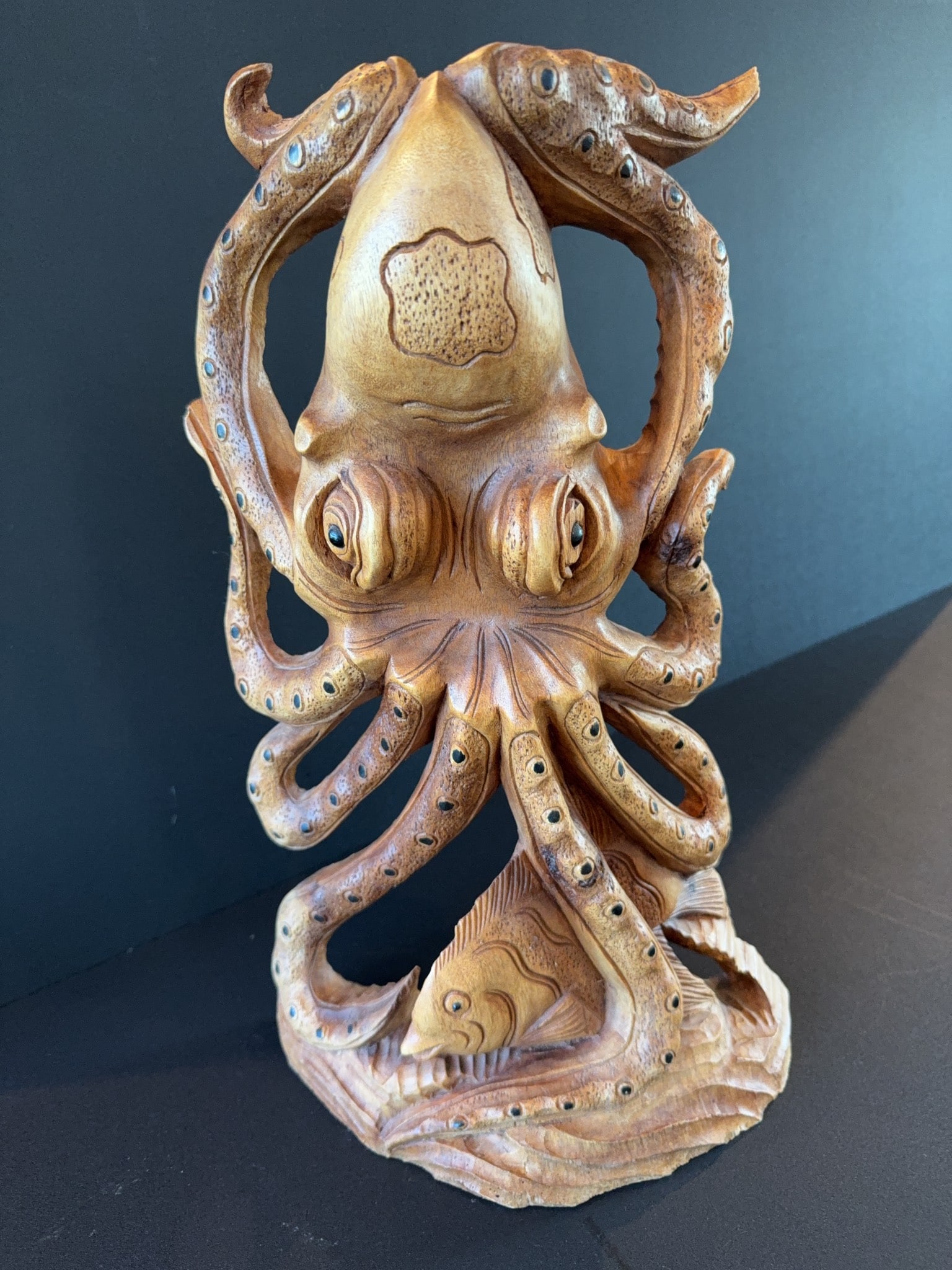 Hand-Carved Wooden Octopus and Fish Sculpture: Hand-carved wooden sculpture depicting an octopus intertwined with a fish. Fine detailing is visible on the tentacles and facial features, with natural wood grain contributing to the unique
