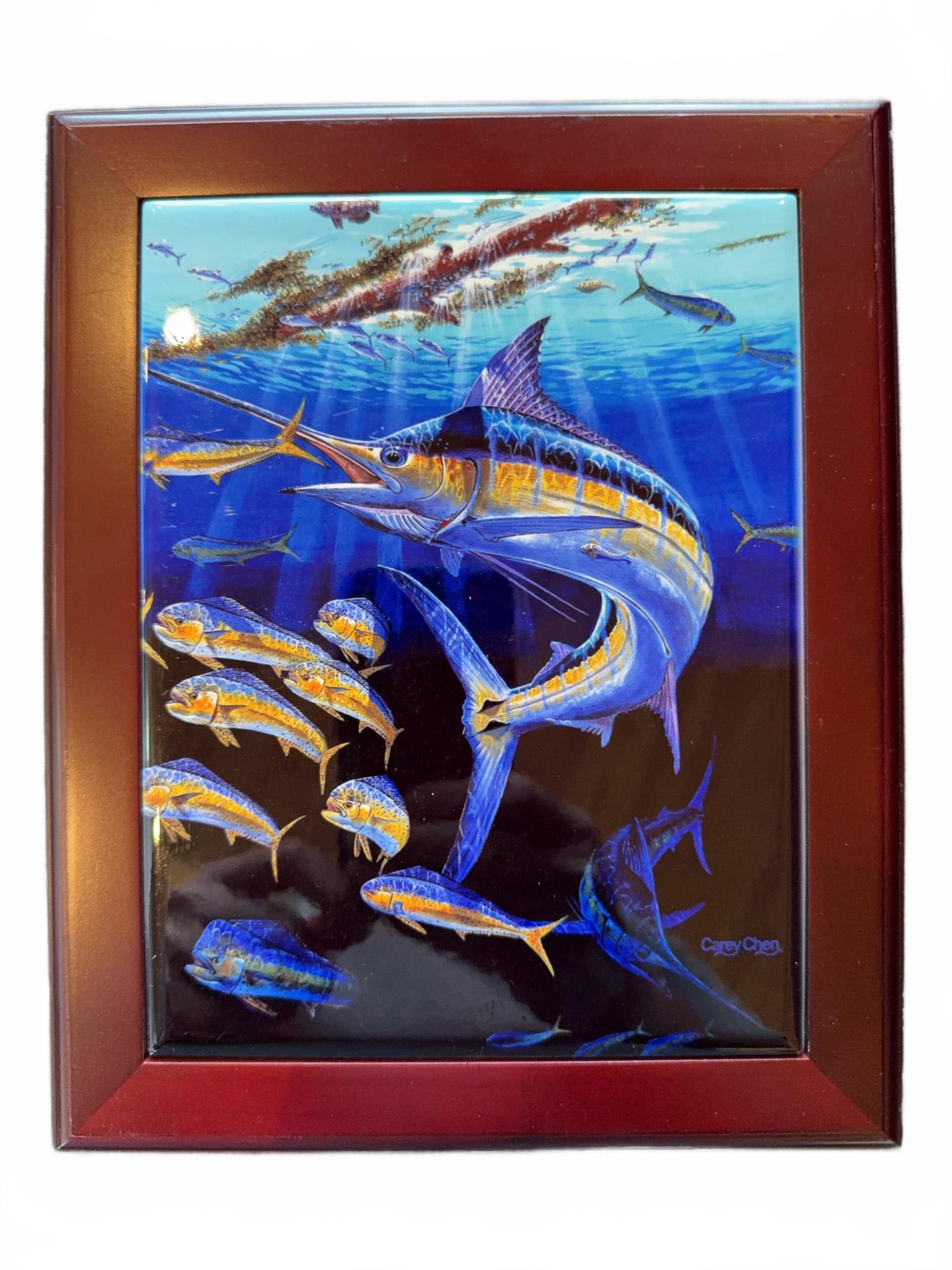 Framed Enamel Art Tile With Marlin and Fish: Enamel-painted art tile featuring a marlin among a school of fish in vivid blue and gold tones, set in a dark wood frame. The piece is signed and measures 8" x 6" according to the label on the back.