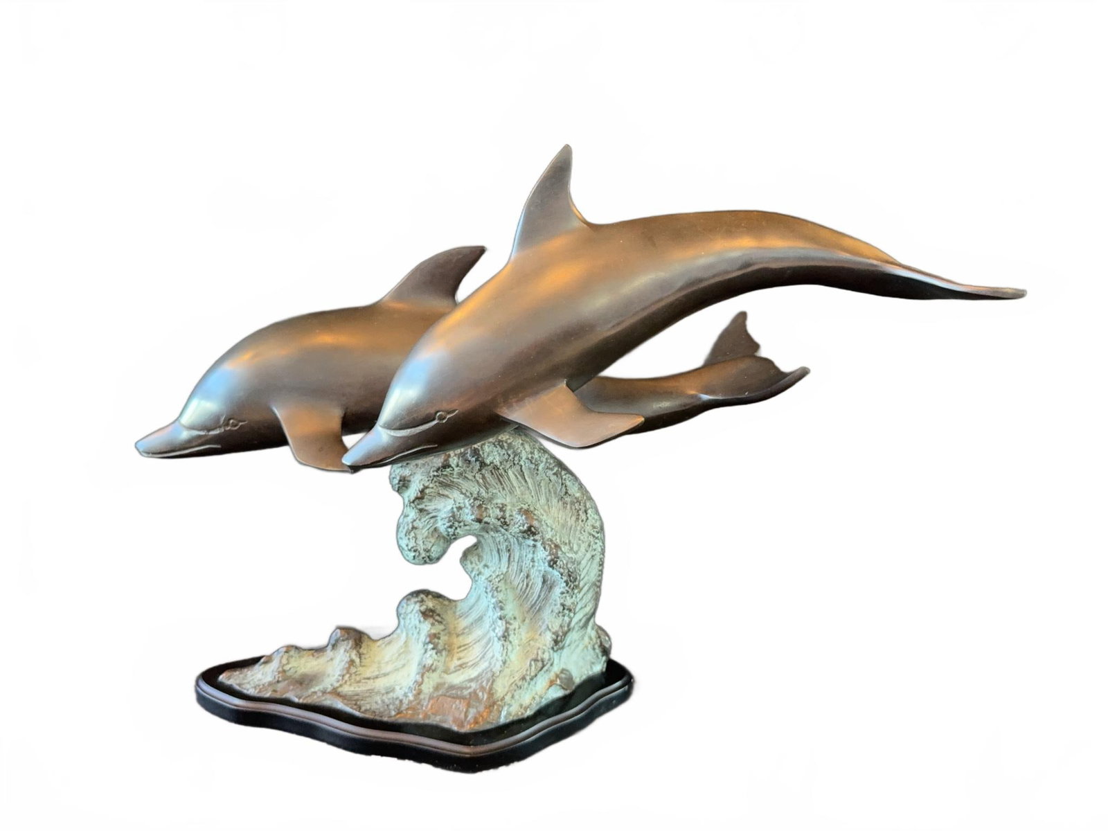 Bronze Sculpture of Two Dolphins on a Wave: Bronze sculpture featuring two dolphins leaping over a stylized wave on a decorative base. The piece showcases smooth bronze work with a contrasting textured wave element, mounted on a contoured base.