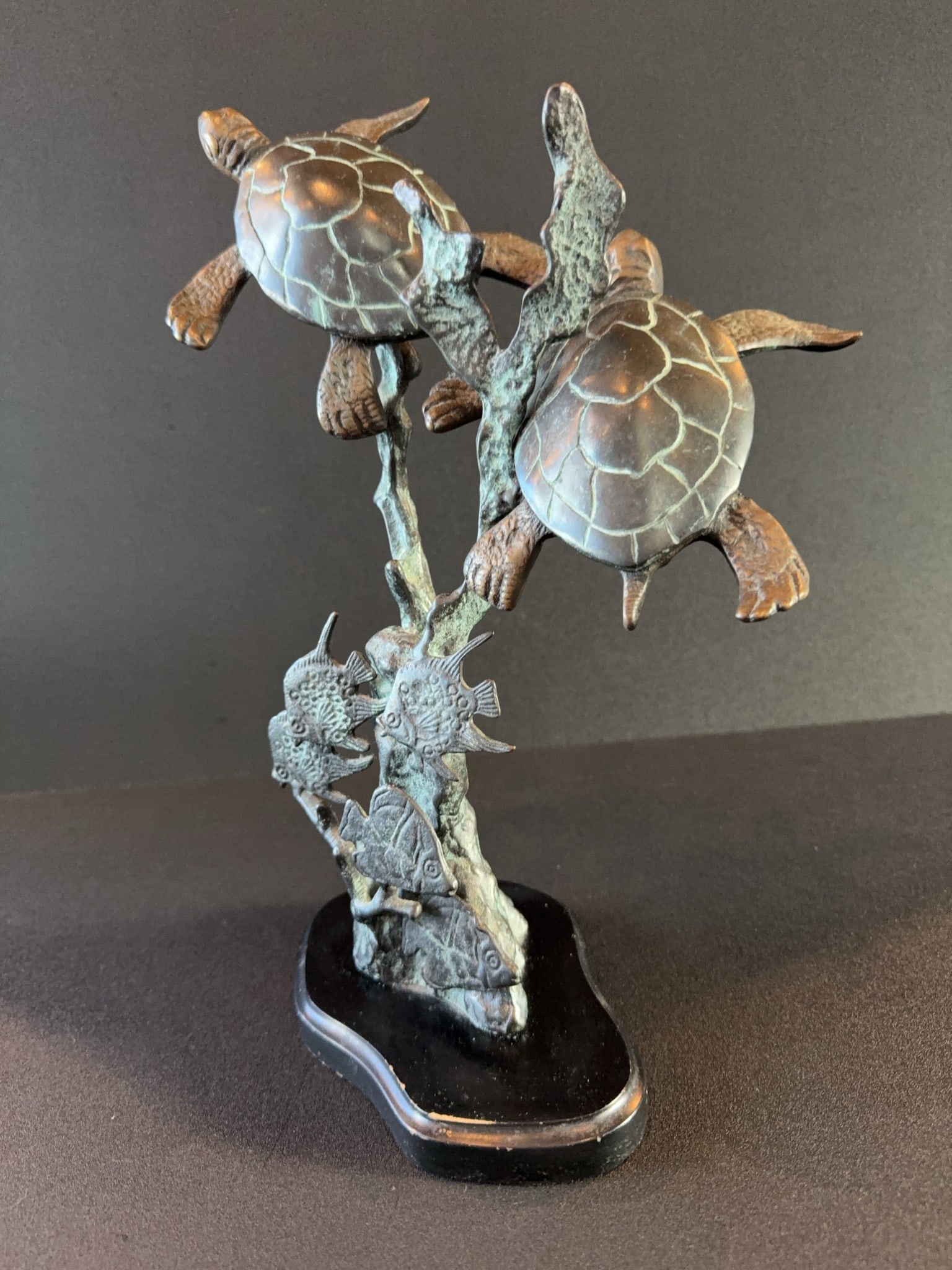 Bronze Sea Turtle Sculpture on Black Base: Bronze sculpture depicting two sea turtles swimming above coral and fish, mounted on a black-shaped base. The piece features detailed turtle shells and marine life, with a patinated finish throughout.