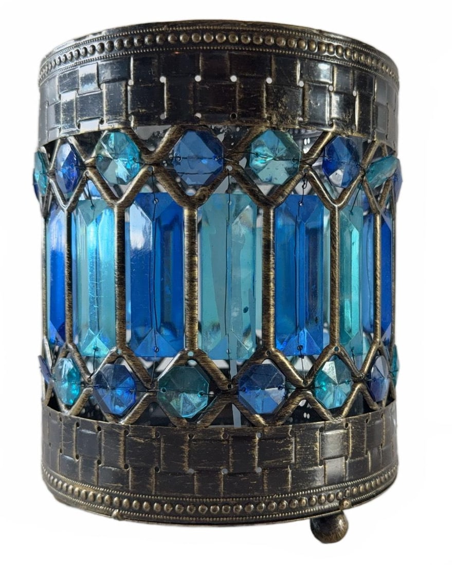 Pier 1 Blue Glass and Metal Candle Holder: Pier 1 candle holder featuring a cylindrical metal frame with faceted blue glass accents in varying shades. Supported by three metal feet. Designed for tealights or small candles. Measures approximate