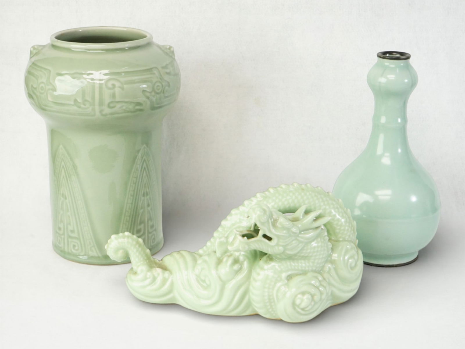 Lot of 3 Asian Celadon Porcelain Pieces: Two Chinese Celadon Vases and a Japanese Celadon Porcelain Dragon, One Vase with Silver-Mounted Rim.Approximate size:vases H:9.5 in,9.25 in,dragon 4.5x5x9 in Shipping: We offer in-house shipping servi