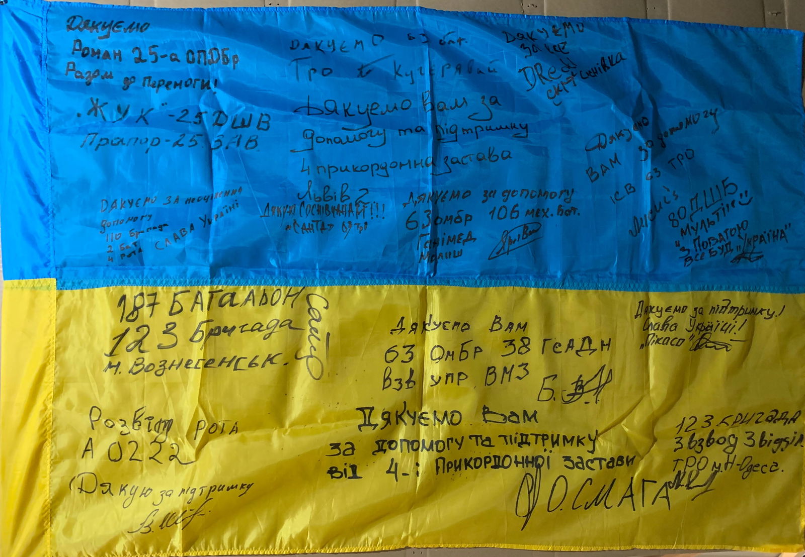 Ukrainian Frontline Flag (Signed by Soldiers): This Ukrainian national flag, bearing numerous handwritten signatures, stands as a deeply personal artifact of the ongoing conflict following the Russian invasion of Ukraine. Created and carried in ac