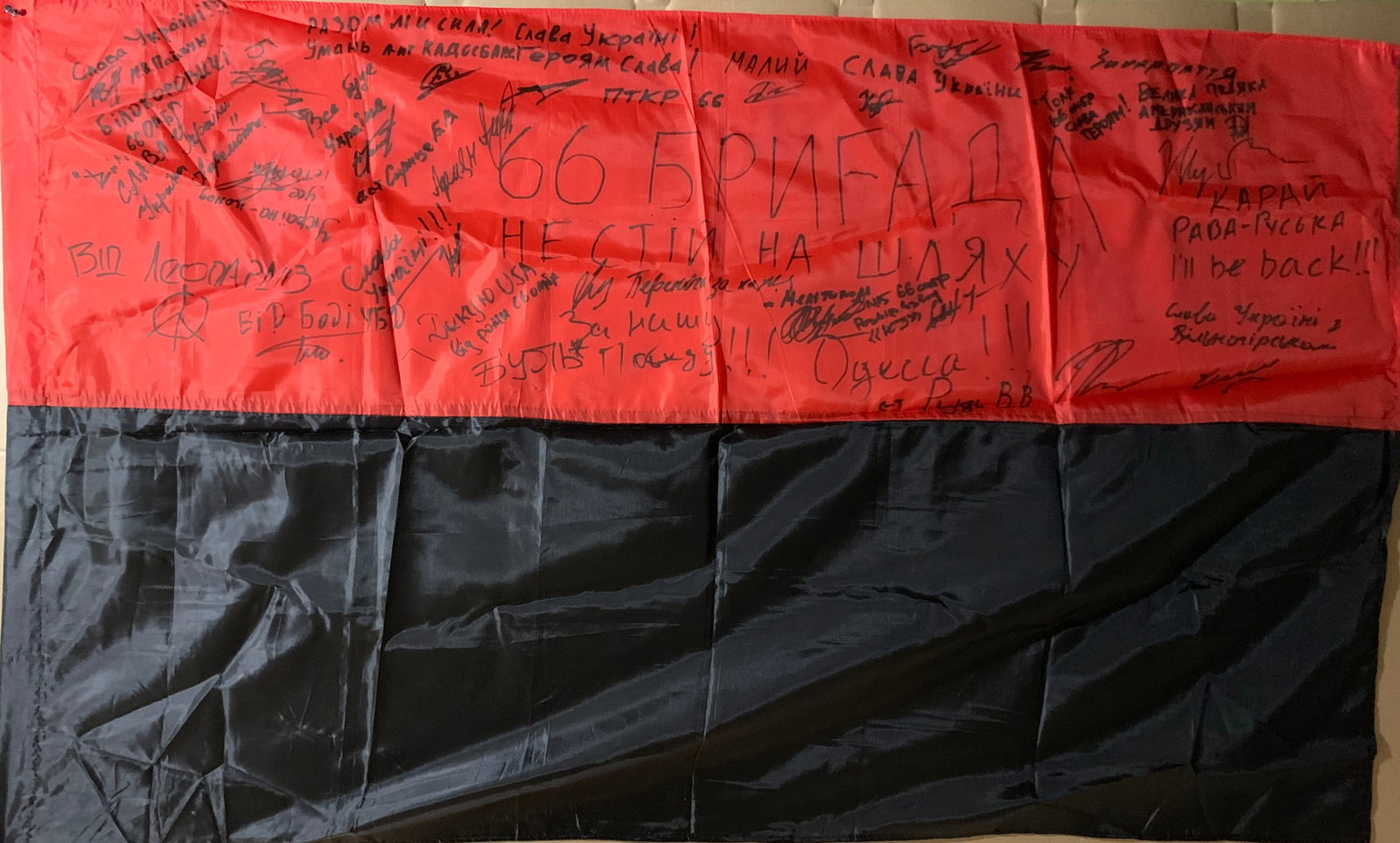 Ukrainian Frontline Flag (Signed by Soldiers): This Ukrainian national flag, bearing numerous handwritten signatures, stands as a deeply personal artifact of the ongoing conflict following the Russian invasion of Ukraine. Created and carried in ac