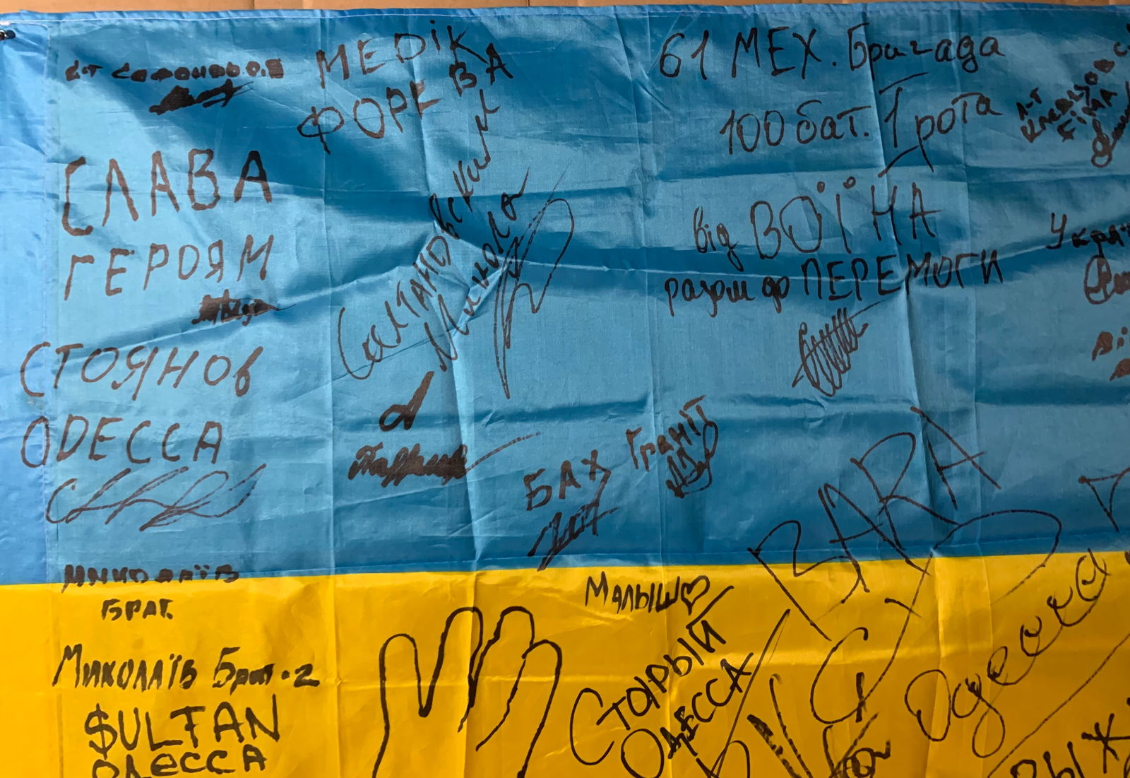Ukrainian Frontline Flag (Signed by Soldiers): This Ukrainian national flag, bearing numerous handwritten signatures, stands as a deeply personal artifact of the ongoing conflict following the Russian invasion of Ukraine. Created and carried in ac