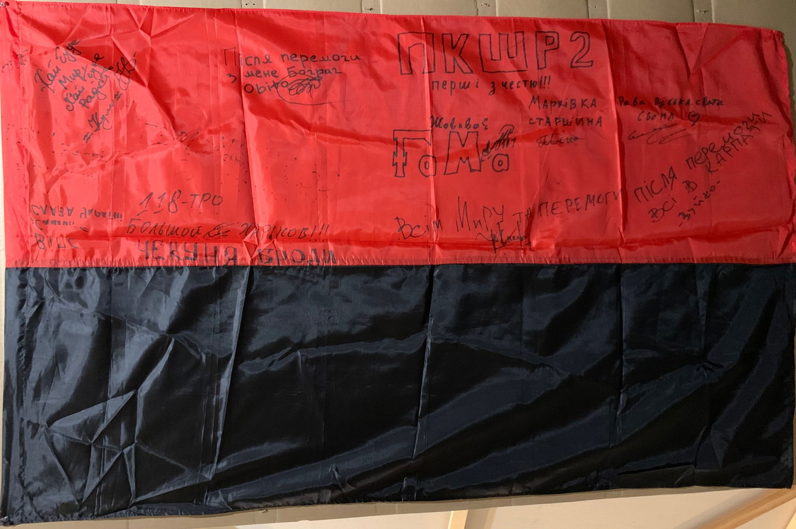 Ukrainian Frontline Flag (Signed by Soldiers): This Ukrainian national flag, bearing numerous handwritten signatures, stands as a deeply personal artifact of the ongoing conflict following the Russian invasion of Ukraine. Created and carried in ac