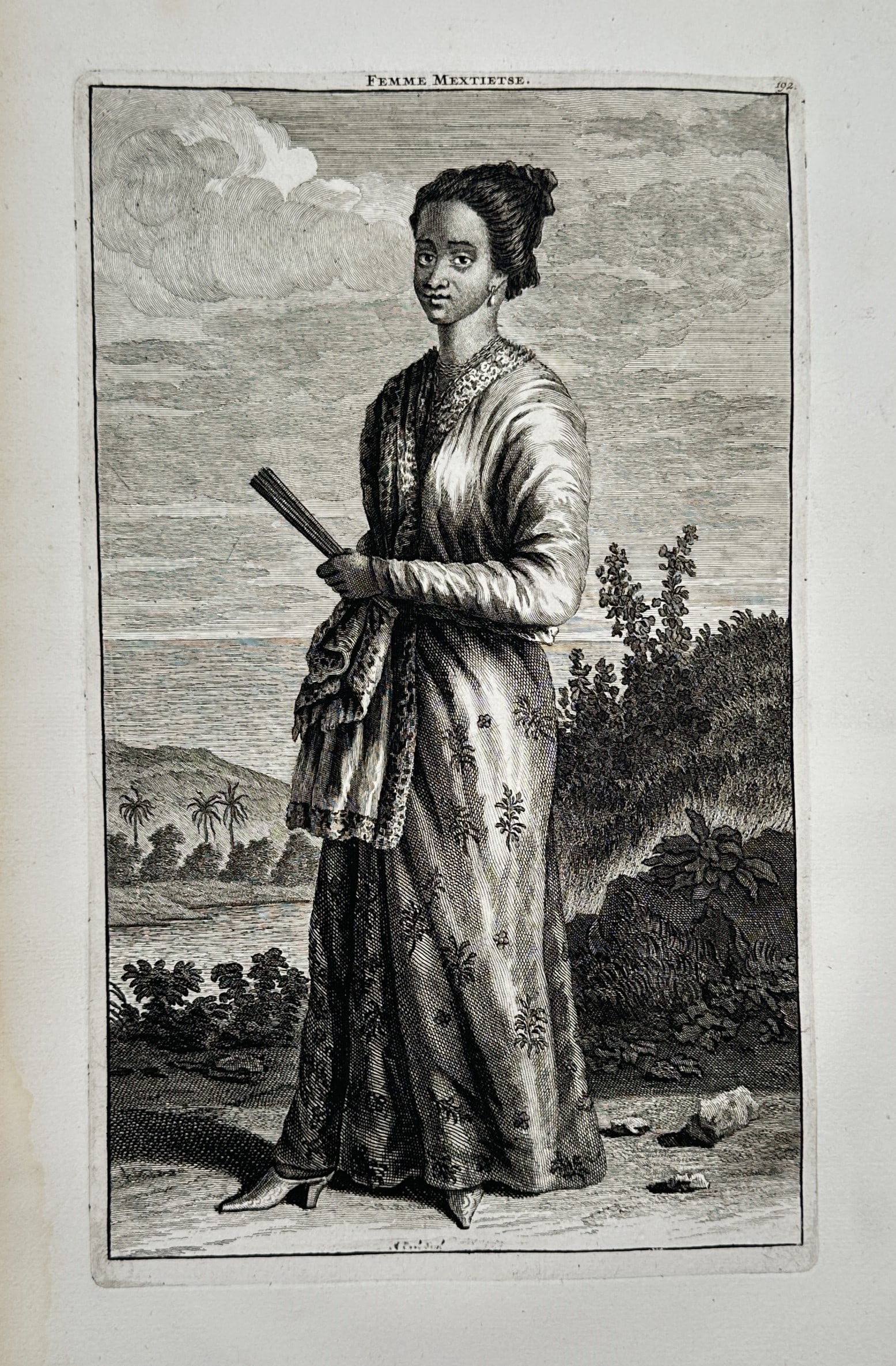Francois Valentijn (1666–1727) – View of a Mixed-Heritage Woman – Copper engraving: "Femme Mextietse" illustrates a full-length portrait of a woman standing in a tropical coastal landscape, holding a folded fan and dressed in an elegantly draped, patterned gown with a lace-trimmed co