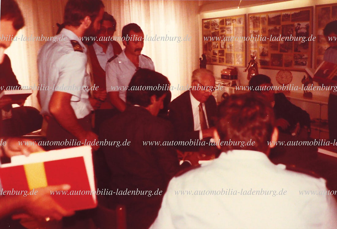 FERRARI Original color photograph of Enzo Ferrari signing his latest book "Ferrari 80", with the: FERRARI Original color photograph of Enzo Ferrari signing his latest book "Ferrari 80", with the pilots of the "Frecce Tricolori" flying squadron as guests, 10x15cm German Description FERRARI original