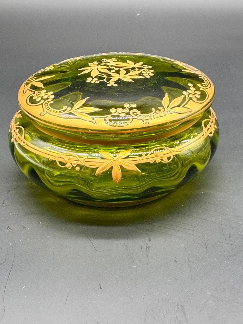 A FINE BOHEMIAN GILT-DECORATED GREEN GLASS BOX AND COVER, LATE 19TH CENTURY: A circular glass box and fitted cover crafted in vibrant transparent green glass, of squat lobed form with molded swirling flutes. Richly hand-decorated in gold leaf with fine botanical sprays on the 