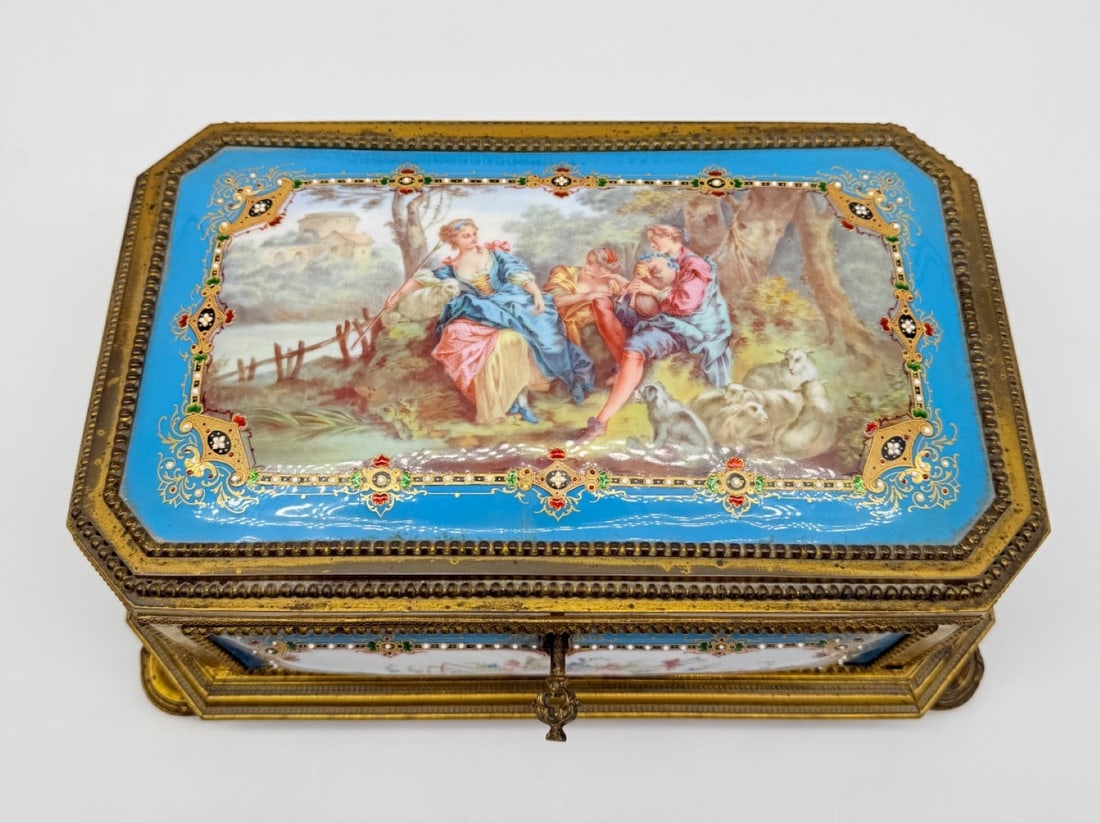 FRENCH GILT-BRONZE AND PORCELAIN CASKET, SIGNED GUITHON BORDEAUX, 19TH CENTURY: A rectangular gilt-bronze casket with cut corners resting on flattened bun feet. The cover is inset with a porcelain plaque hand-painted with a pastoral, gallant scene of figures in 18th-century attir