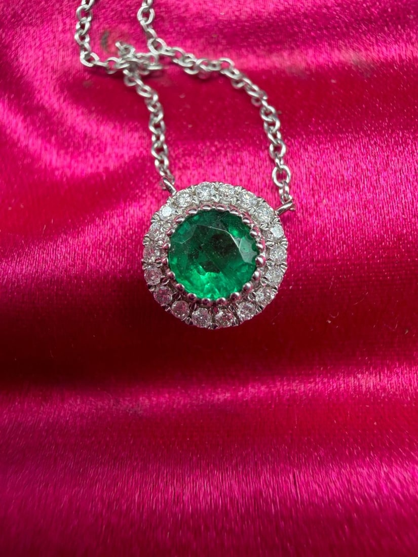 18K white gold necklace set with a Colombian emerald and brilliant-cut diamonds: 18K white gold (750/1000) necklace holding a circular pendant centered with a bezel-set round-cut Colombian emerald, within a brilliant-cut diamond pave halo.Fine cable chain with a spring ring clasp.