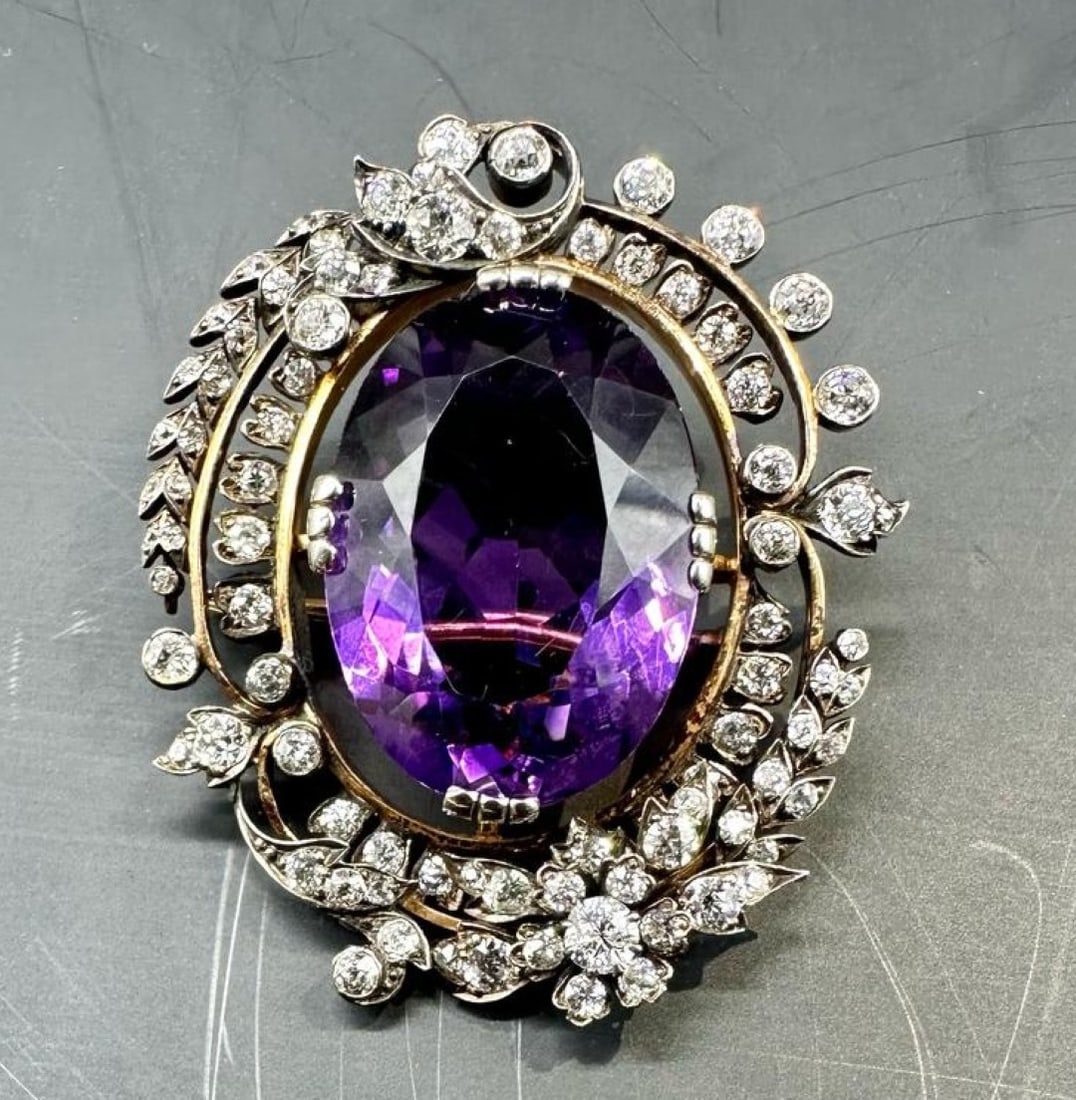 Victorian Large Gold Brooch With Large Amethyst And Diamonds: A striking antique floral-style brooch in 14K rose gold and white gold (585/1000). It is centred on a magnificent oval-cut amethyst set in a claw setting, set off by an asymmetrical openwork frame fea