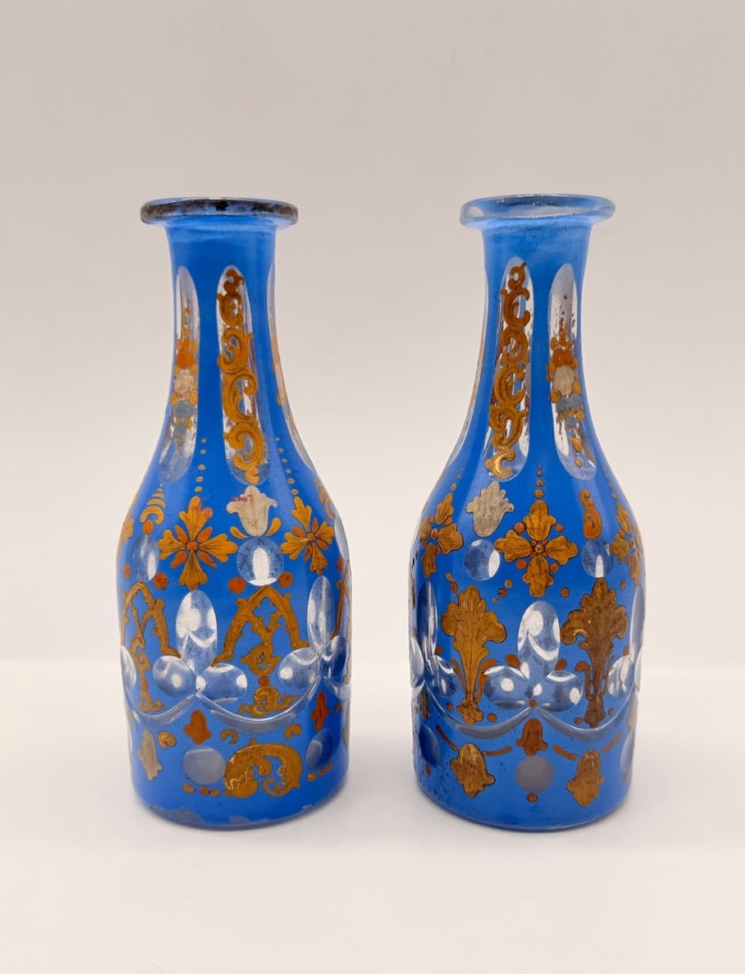 PAIR OF BOHEMIAN ENAMELED GLASS BOTTLES FOR THE ORIENTAL MARKET, 19TH CENTURY: A pair of Bohemian glass bottles featuring cobalt blue overlay cut to clear, decorated with hand-painted polychrome enamel and gilt scrolls. The elongated necks and cylindrical bodies display cut oval