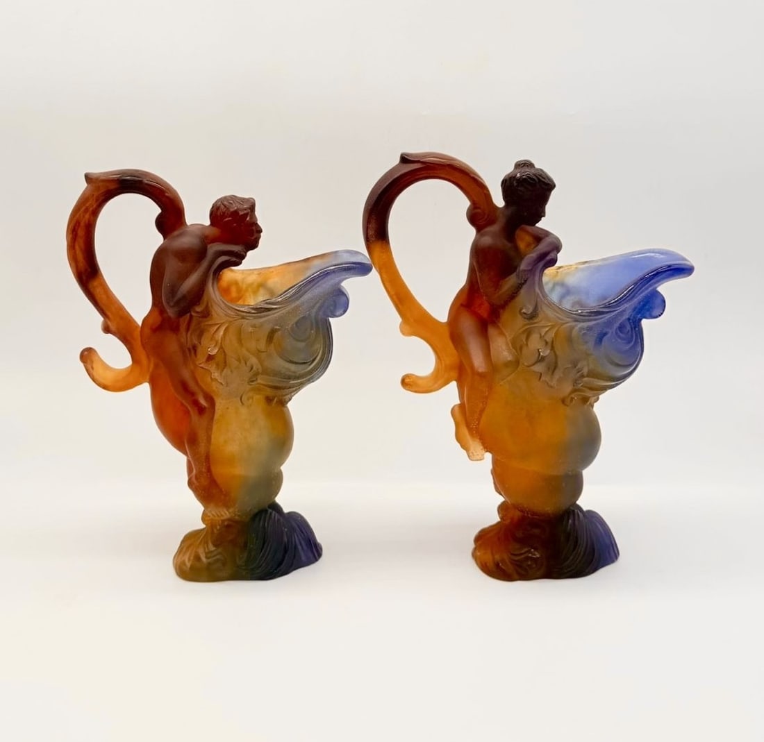 PAIR OF DAUM NANCY PÂTE DE VERRE MYTHOLOGICAL EWERS, 20TH CENTURY: A pair of sculptural pâte de verre glass ewers crafted with mythological figural motifs. Each ewer features a organic shell-form spout transitioning into an amber-to-blue gradient body, supported by 