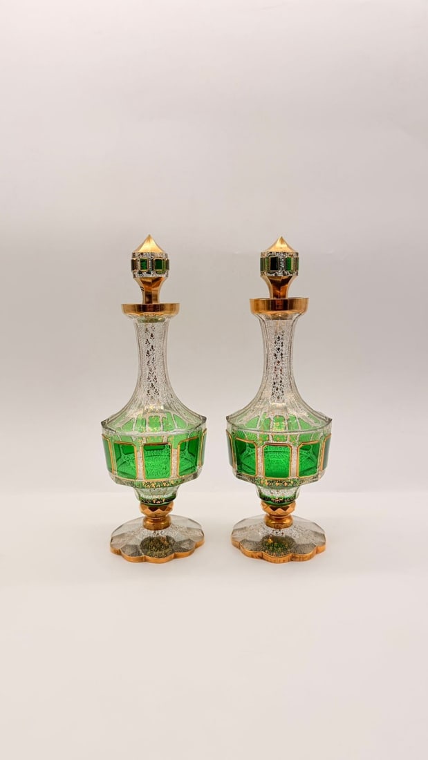 PAIR OF LARGE MOSER CUT AND GILDED GLASS CABOCHON DECANTERS, 19TH CENTURY: A pair of footed glass decanters featuring emerald green overlay panels cut to clear clear crystal with geometric cabochons (window cutouts). The clear glass sections are embellished with gilded scrol