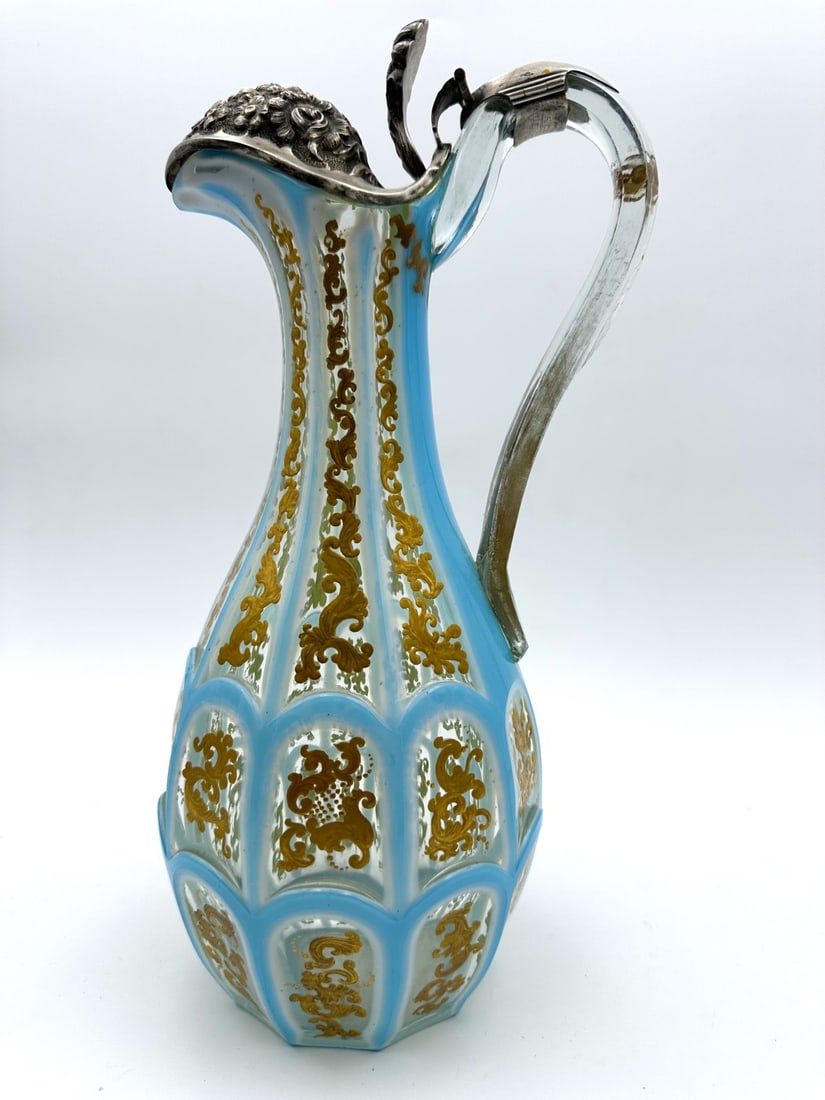FRENCH OPALINE DOUBLE OVERLAY GLASS JUG WITH SILVER MOUNT, CHARLES X PERIOD, CIRCA 1820–1830: Double overlay glass jug featuring sky-blue opaline over white milk glass cut to clear crystal. The body is worked with vertical panel facets and arched window cutouts (fenêtres), heavily decorated w