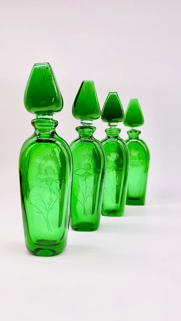 SET OF FOUR BOHEMIAN EMERALD GREEN ENGRAVED GLASS DECANTERS, MANUFACTURE MOSER, EARLY 20TH CENTURY: A set of four graduated decanters or scent bottles in deep emerald green glass. Each piece features a flat-sided oval body and a faceted rim, topped with a matching tear-shaped, faceted stopper. The b