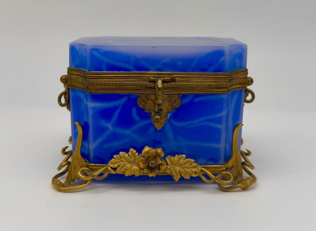 FRENCH BLUE OPALINE GLASS BOX WITH GILT-BRONZE MOUNTS, 19TH CENTURY: An octagonal hinged casket in vibrant blue opaline glass with subtle marbling. The box is set within a chased gilt-bronze frame featuring a hinged rim mount, a decorative front clasp, side ring handle