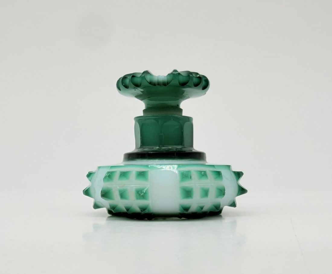 FRENCH EMERALD GREEN AND OPALINE DOUBLE OVERLAY GLASS PERFUME BOTTLE, CIRCA 1840–1850: A miniature squat perfume bottle crafted in cased double overlay glass. The body consists of clear crystal layered with opaque white opaline and topped with an emerald green glass casing. The squat, c