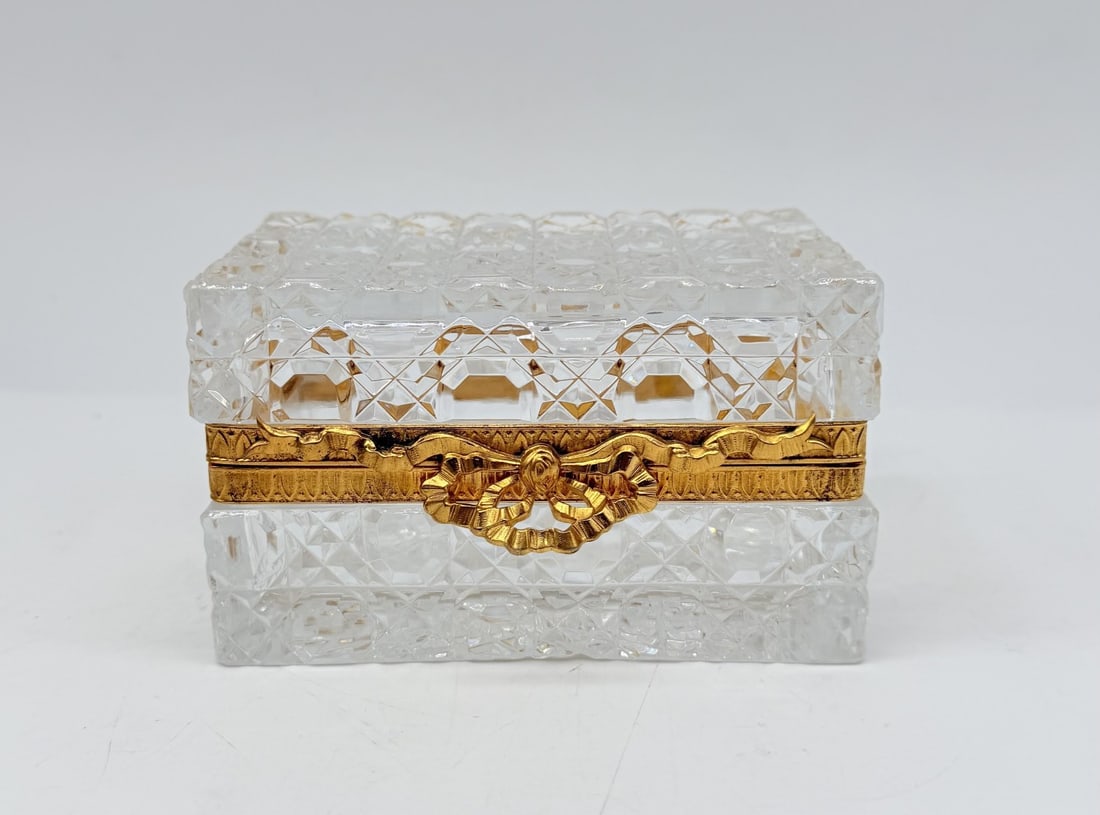 FRENCH CUT CRYSTAL CASKET BOX WITH GILT-BRONZE BOW CLASP, LATE 19TH CENTURY: A large rectangular hinged casket box crafted in clear, heavy lead crystal. The entire exterior—including the lid, base, and sides—is decorated with deep diamond-point (diamants biseaux) cutting. 
