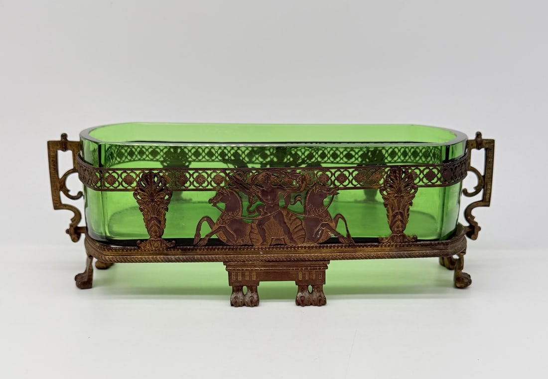 FRENCH GREEN GLASS JARDINIÈRE CENTERPIECE WITH GILT-BRONZE FIGURAL MOUNTS, NAPOLEON III PERIOD: An elongated rectangular centerpiece or jardinière in vivid emerald green glass with rounded corners. The glass liner rests within an intricate bronze frame featuring openwork geometric lattice borde