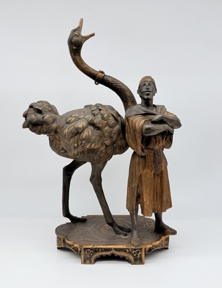 FRENCH COLD-PAINTED SPELTER MODEL OF AN ARAB FIGURE WITH AN OSTRICH, CIRCA 1890: A large French cold-painted spelter sculpture depicting a North African or Arab handler standing beside an ostrich. The figure stands with arms crossed, dressed in a draped tunic highlighted with warm