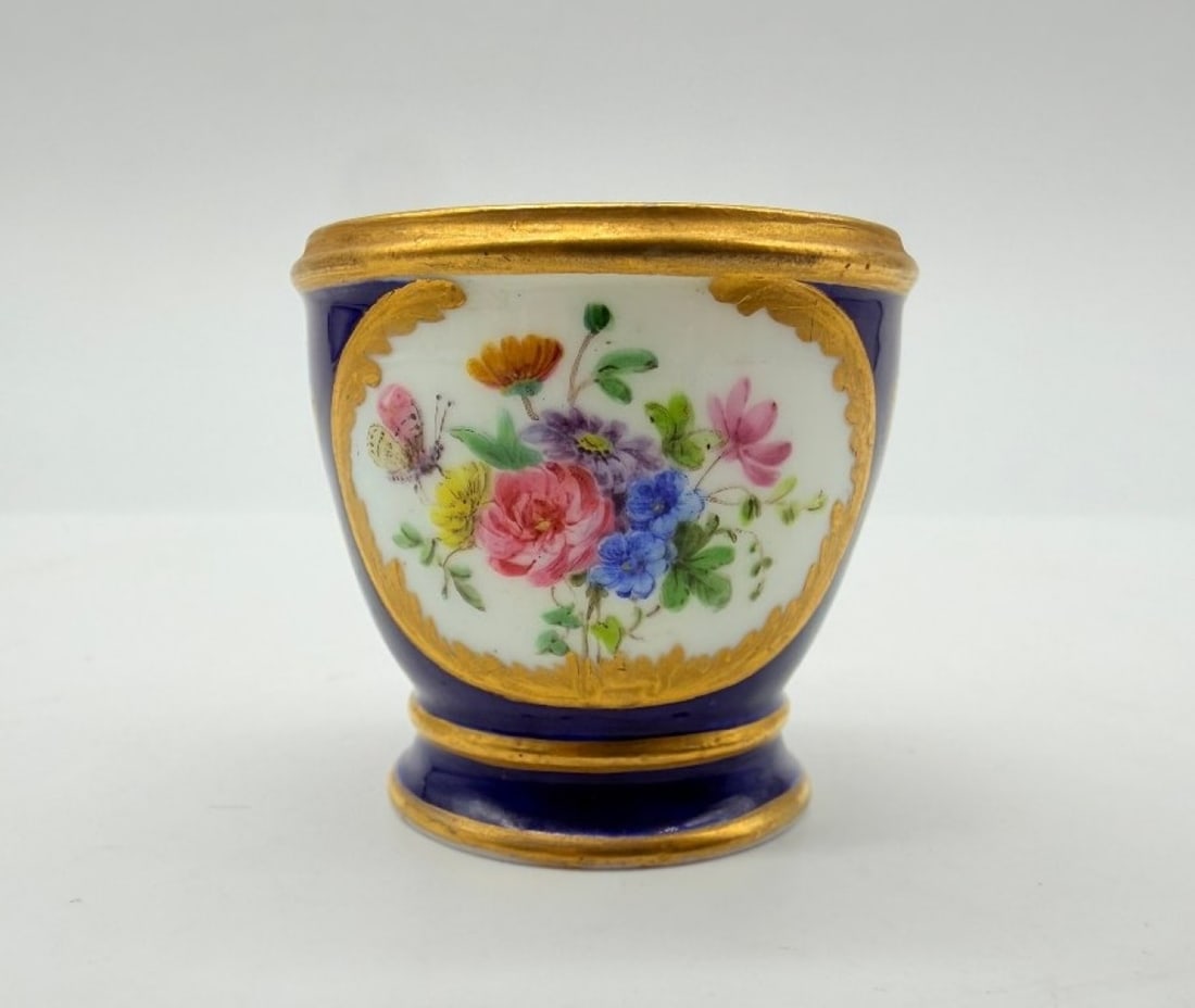 Sèvres, After, Blue Ground Porcelain Cup With Floral Decoration, Louis XV Style: Sèvres, (After)Sèvres porcelain goblet with a blue ground, featuring a gold rocaille and foliage border enclosing a bouquet of polychrome flowers and insects.Louis XV style.H_4.5 cmIn good overall c
