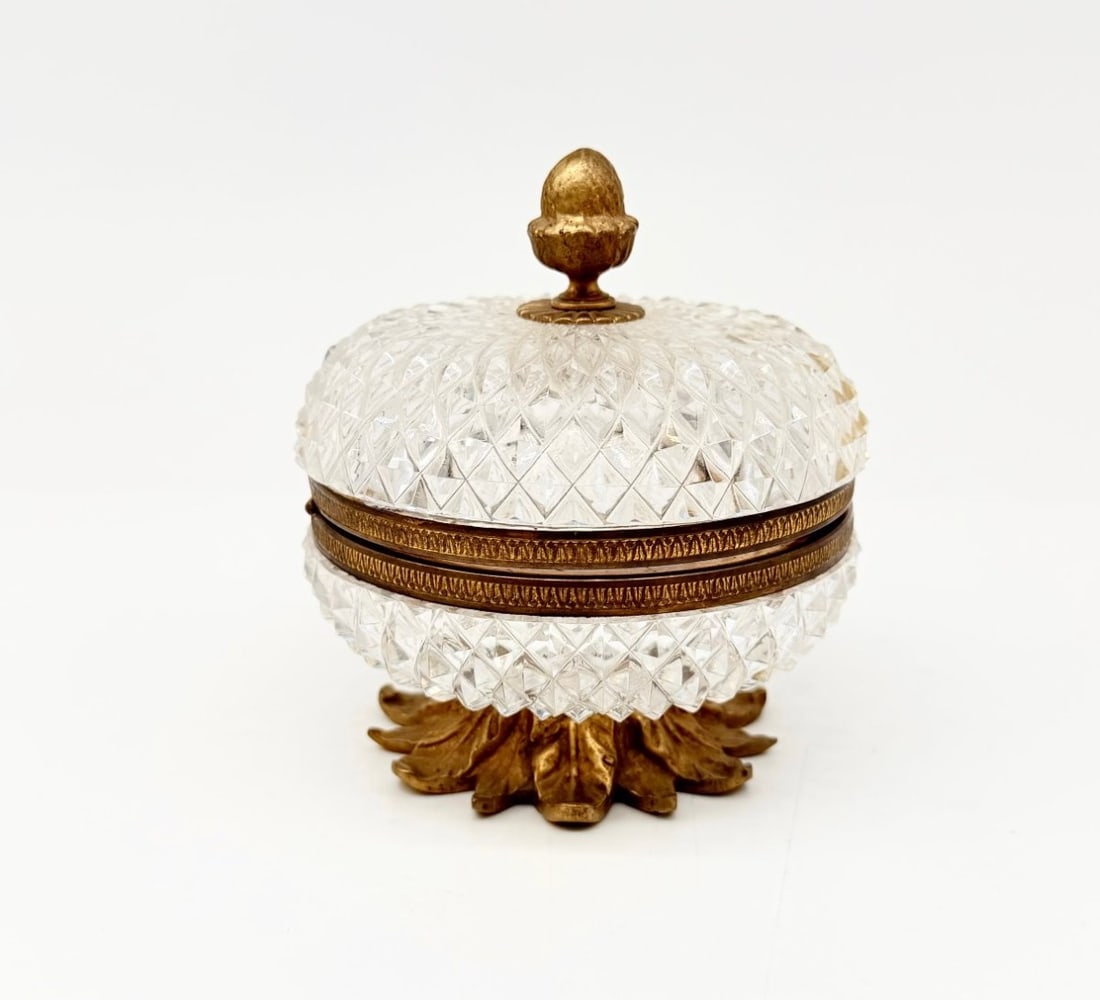 Cut Crystal And Gilt Bronze Covered Box On Pedestal, Charles X Period: A circular lidded box on a pedestal, made of diamond-cut crystal; the frame and band are in gilded bronze chiselled with geometric motifs; the lid is topped with an acorn-shaped knob; the base is comp