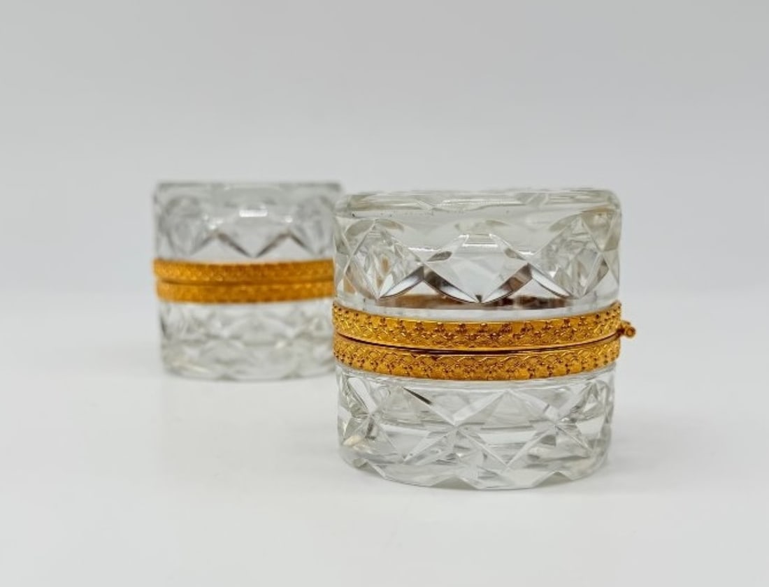 Baccarat, Pair Of Cut Crystal And Gilt Bronze Covered Boxes: BACCARATPair of small, lidded, cylindrical boxes in diamond-cut crystal, with a gilded bronze mount chased with a pearl frieze.France. Late 19th century.H_6 cm W_6 cmIn perfect condition