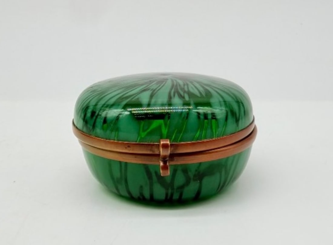 Murano Green Glass Box With Marbled Decoration, Italy, 20th Century: A circular box (or powder jar) made of green-tinted Murano glass with inclusions of dark, sinuous filaments forming a mottled or marbled pattern, opening via a central hinged mount in gilded brass.Ita
