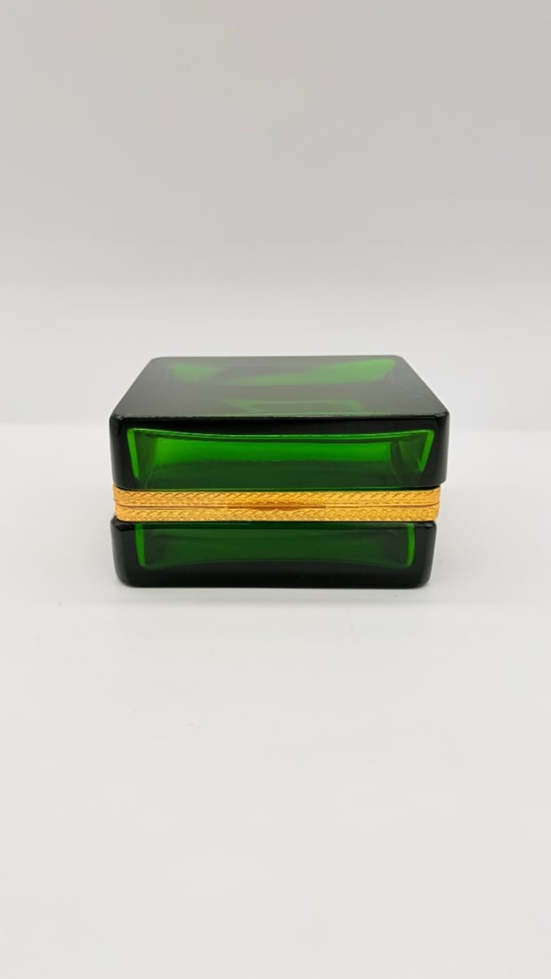 FRENCH GREEN GLASS SQUARE CASKET BOX WITH GILT-BRONZE MOUNTS, ART DECO PERIOD: A square hinged casket box in polished emerald-green glass featuring thick, faceted side walls and clean geometric lines. The box is fitted with a finely chased gilt-bronze (ormolu) hinged rim mount a